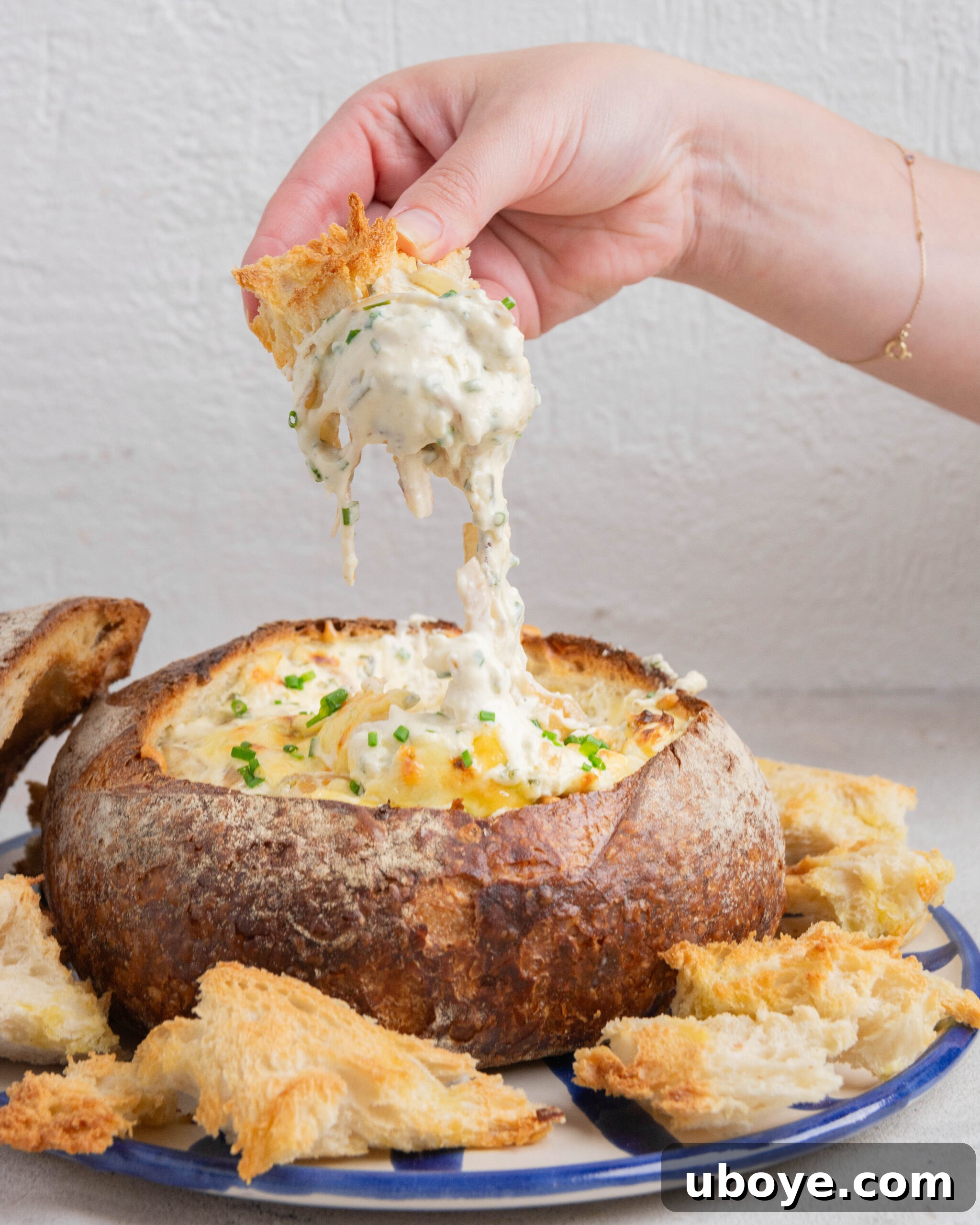 A large piece of bread being dipped into a French onion dip cob loaf, showing the creamy dip inside.