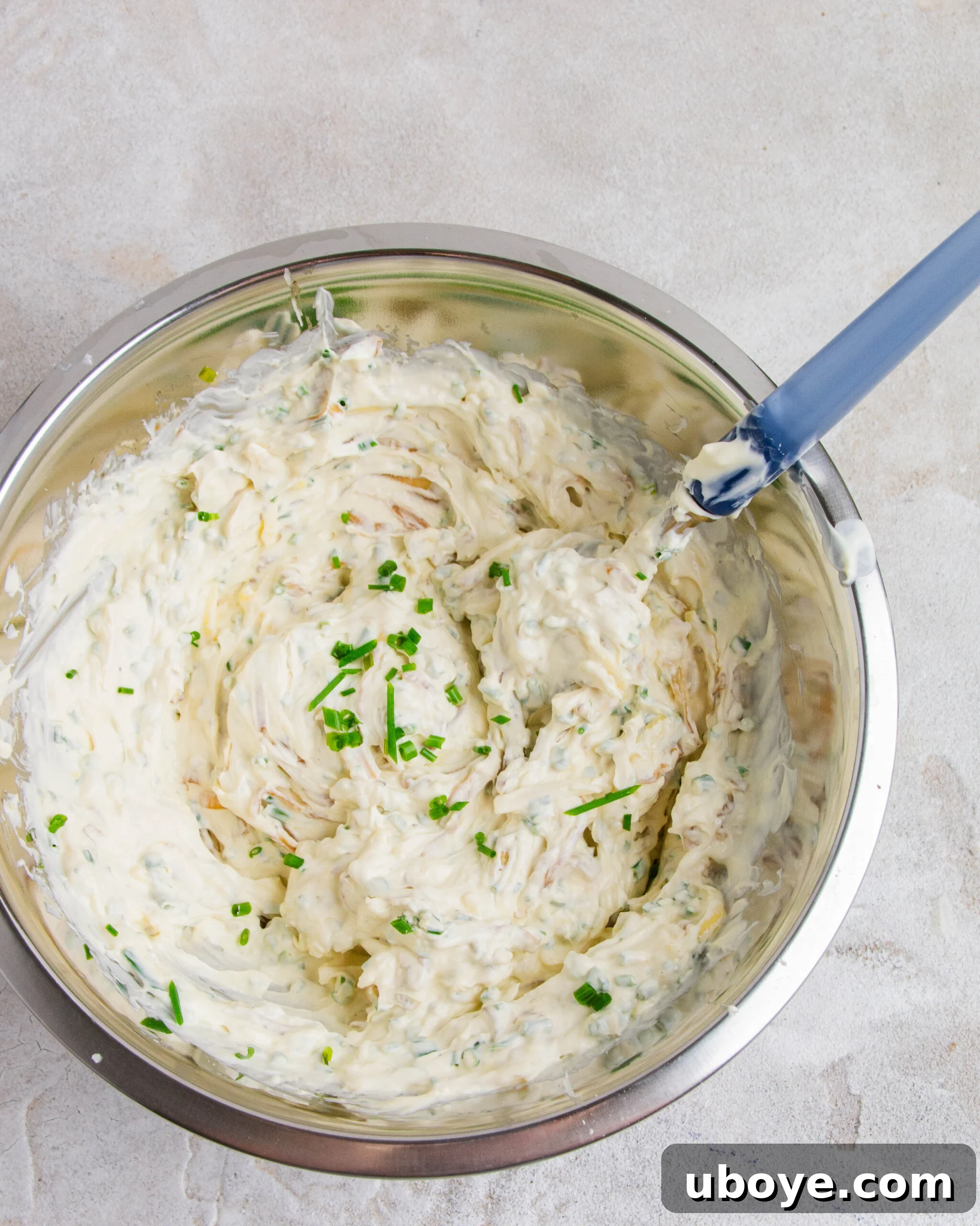 A stainless steel bowl containing the creamy French onion dip filling, with a blue spoon resting in it.