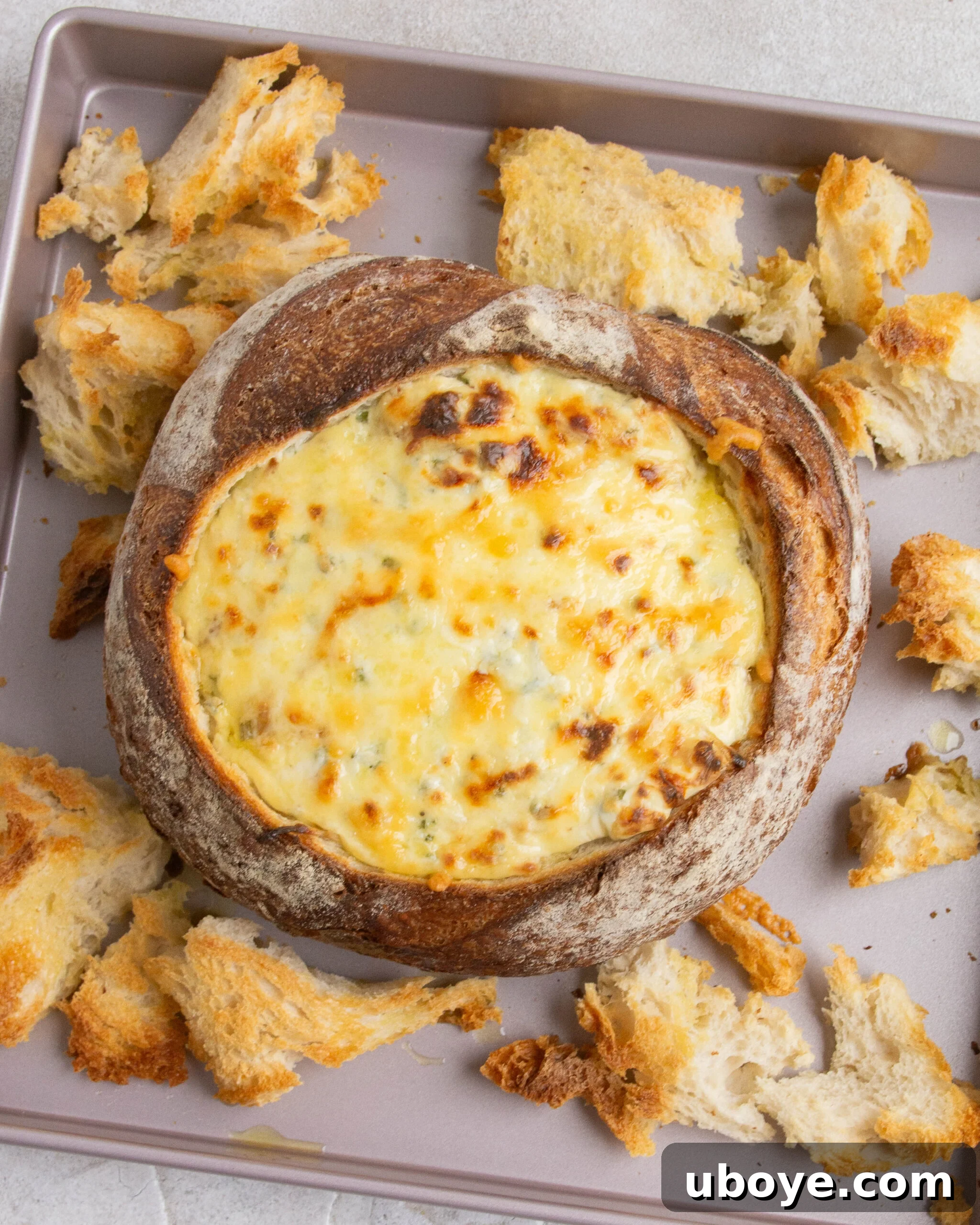 A baked French onion dip cob loaf on a baking tray, with golden-brown bread pieces scattered around it.