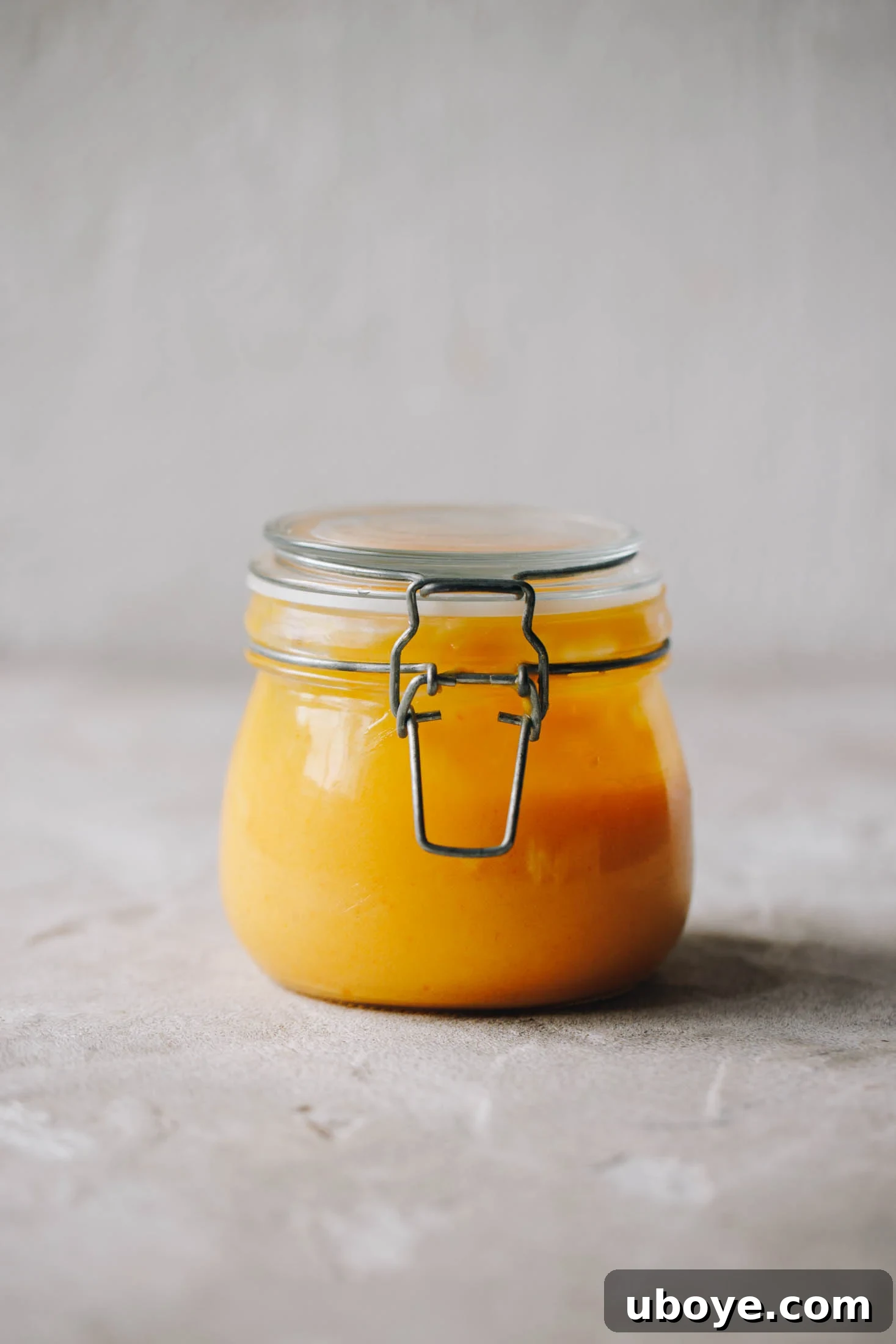 A close-up shot of a clear glass jar filled with luscious homemade lemon curd, ready for storage.