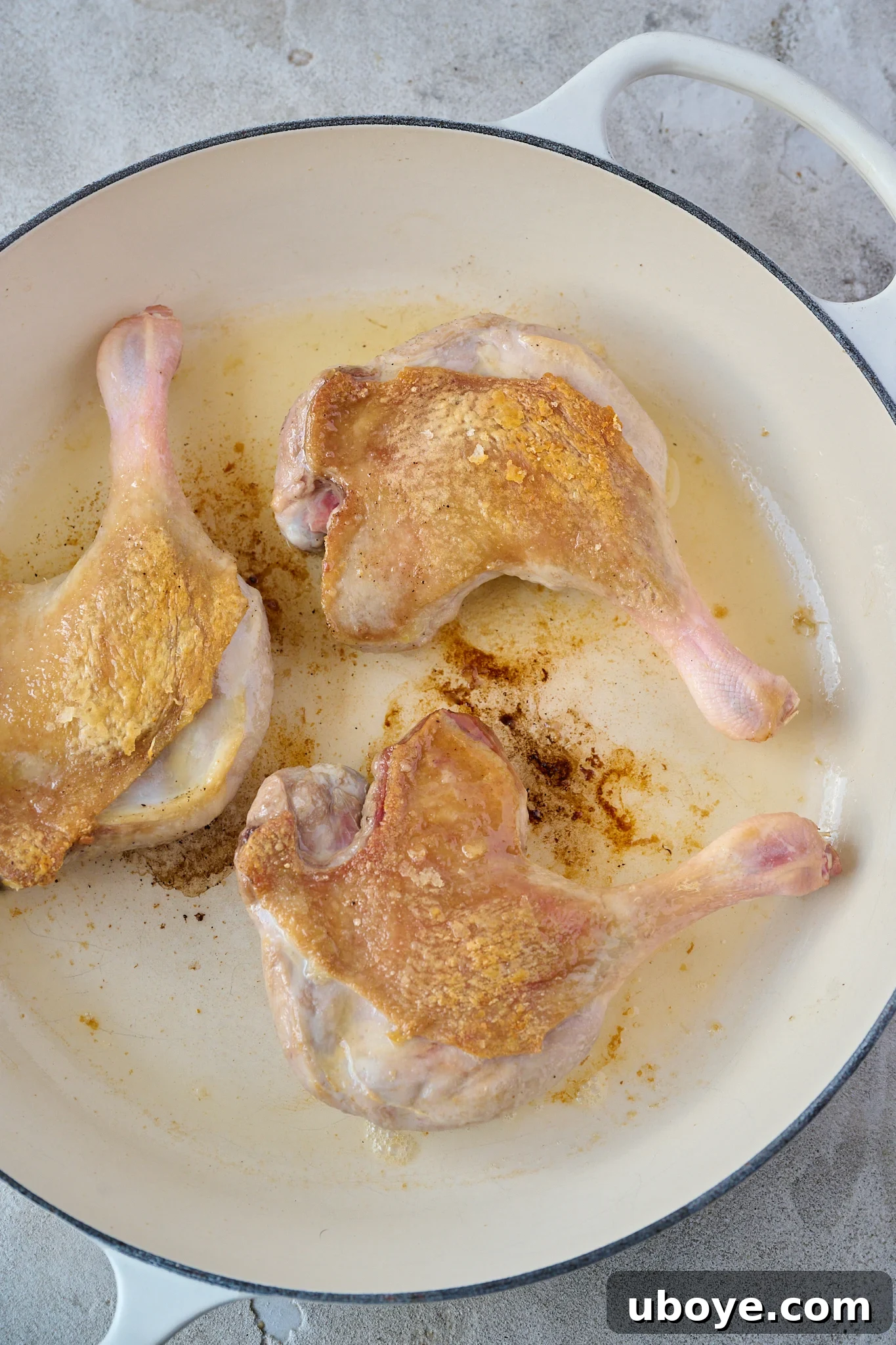 Three duck legs are in a white pan and have crispy skin. 