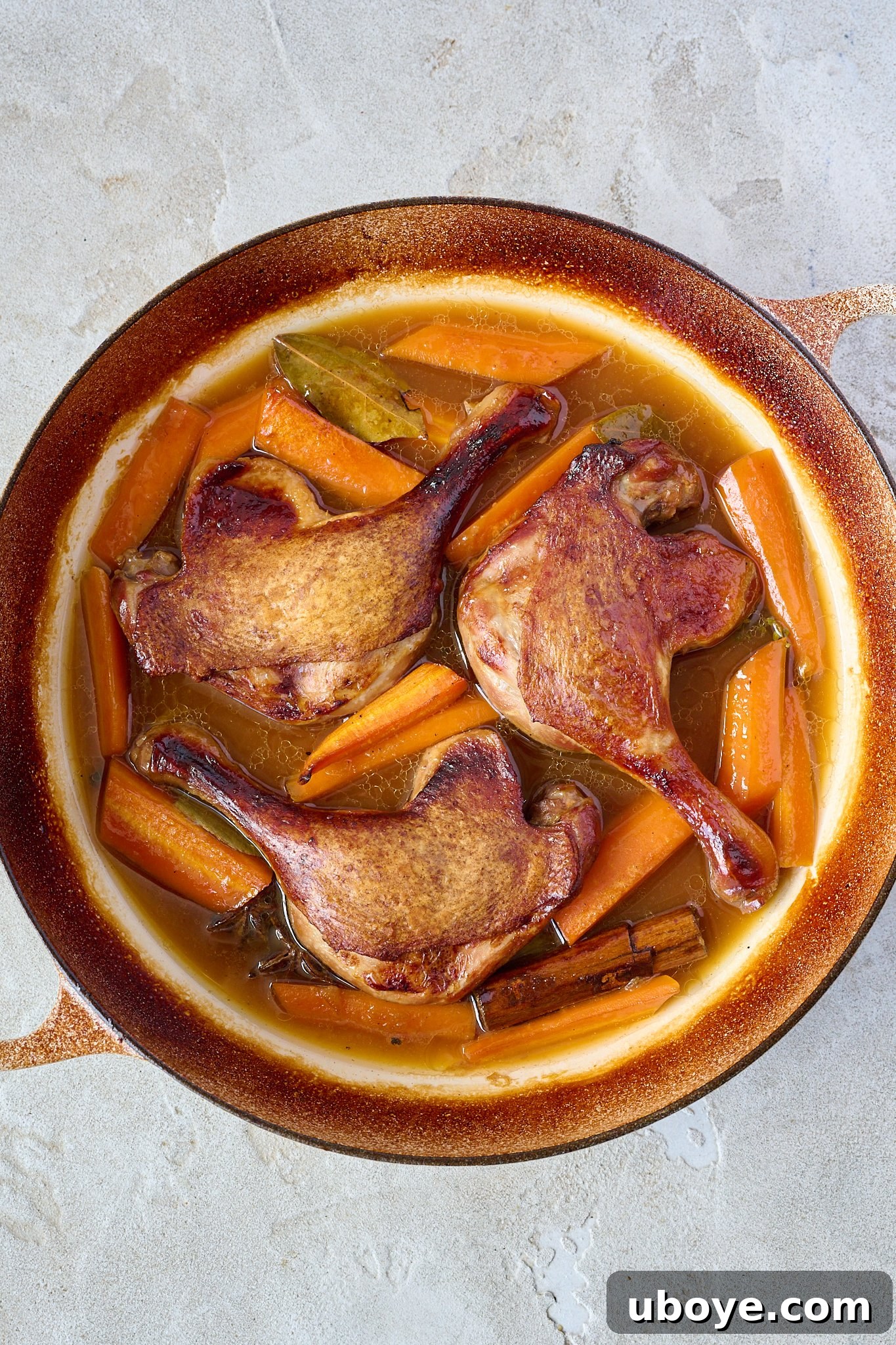Crispy duck legs are shown in a white pan with brown sauce and carrots. 