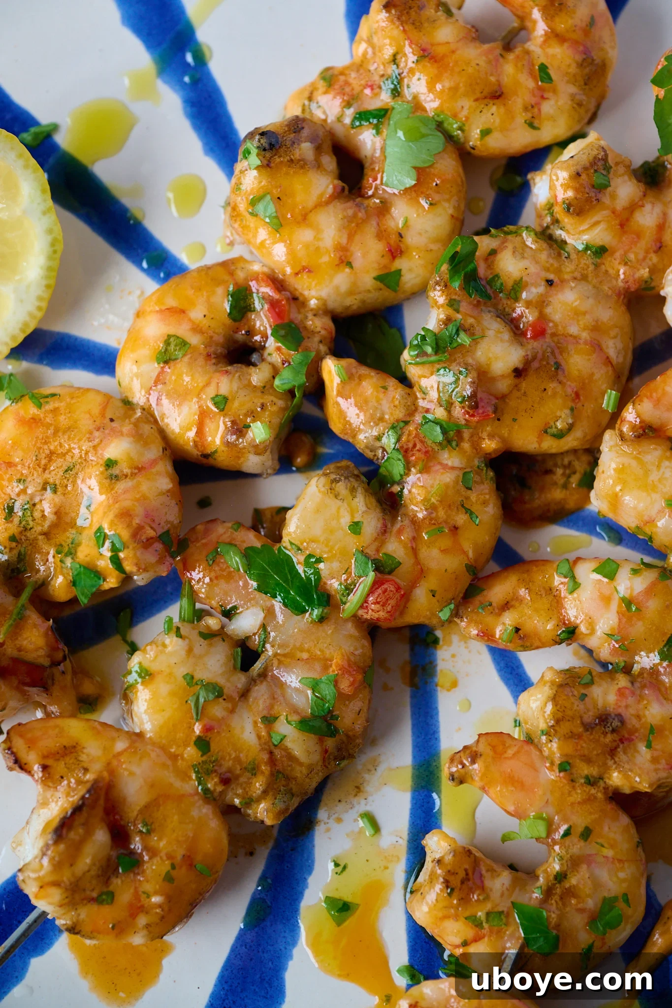 Smoky Grilled Shrimp Skewers with Zesty Tomato Butter 9 Grilled Shrimp Skewers with Tomato Butter (BBQ Prawns) are on blue and white striped plate with fresh parsley sprinkled over.