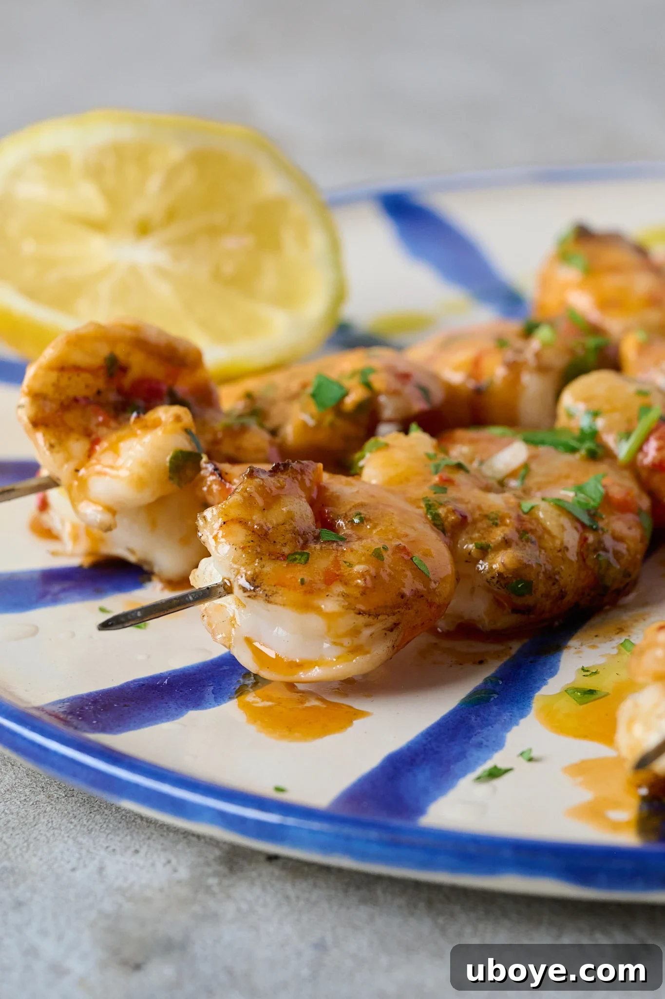 Smoky Grilled Shrimp Skewers with Zesty Tomato Butter 10 Grilled Shrimp Skewers with Tomato Butter (BBQ Prawns) are on blue and white striped plate with fresh parsley sprinkled over. A lemon sits on the in the left side of the plate.