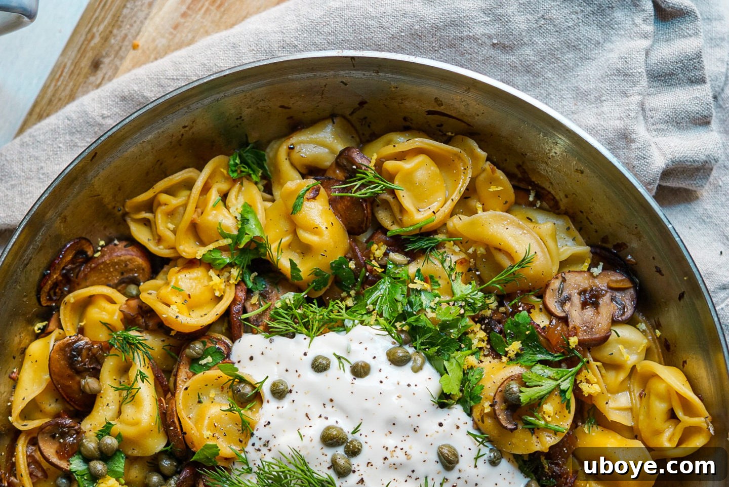Close-up of a bowl of creamy vegan garlic mushroom tortellini, garnished with fresh dill and lemon zest.
