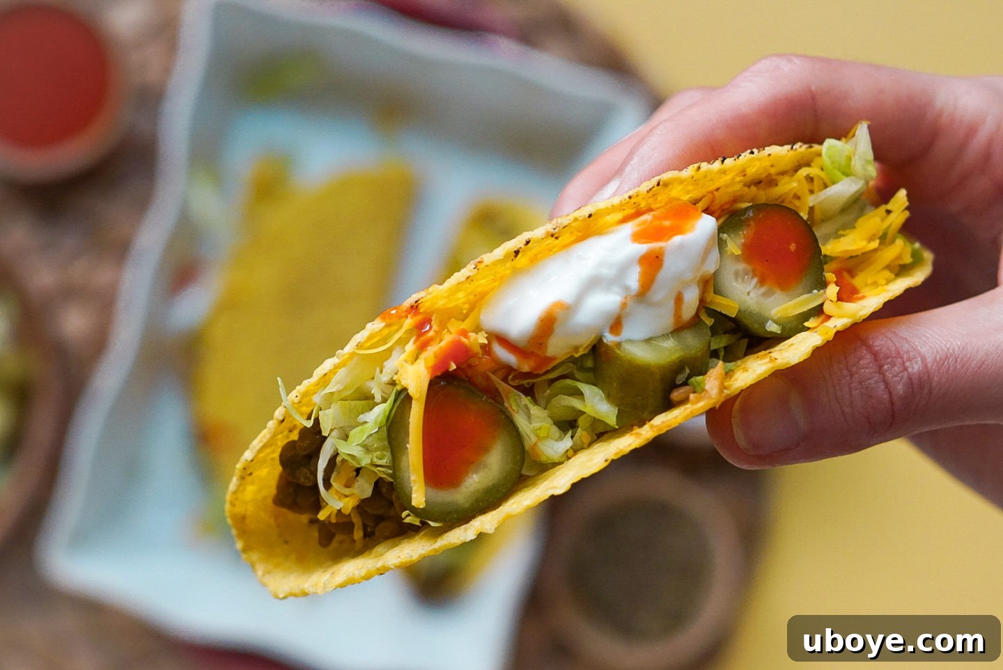 Dill Pickle Plant-Based Beef Tacos 6 Close-up shot of hands assembling a vegan beef and pickle taco with all the fresh toppings
