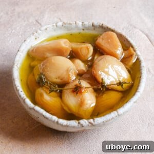 A beautiful glass jar filled with golden garlic confit cloves and infused olive oil, ready for storage or immediate use.