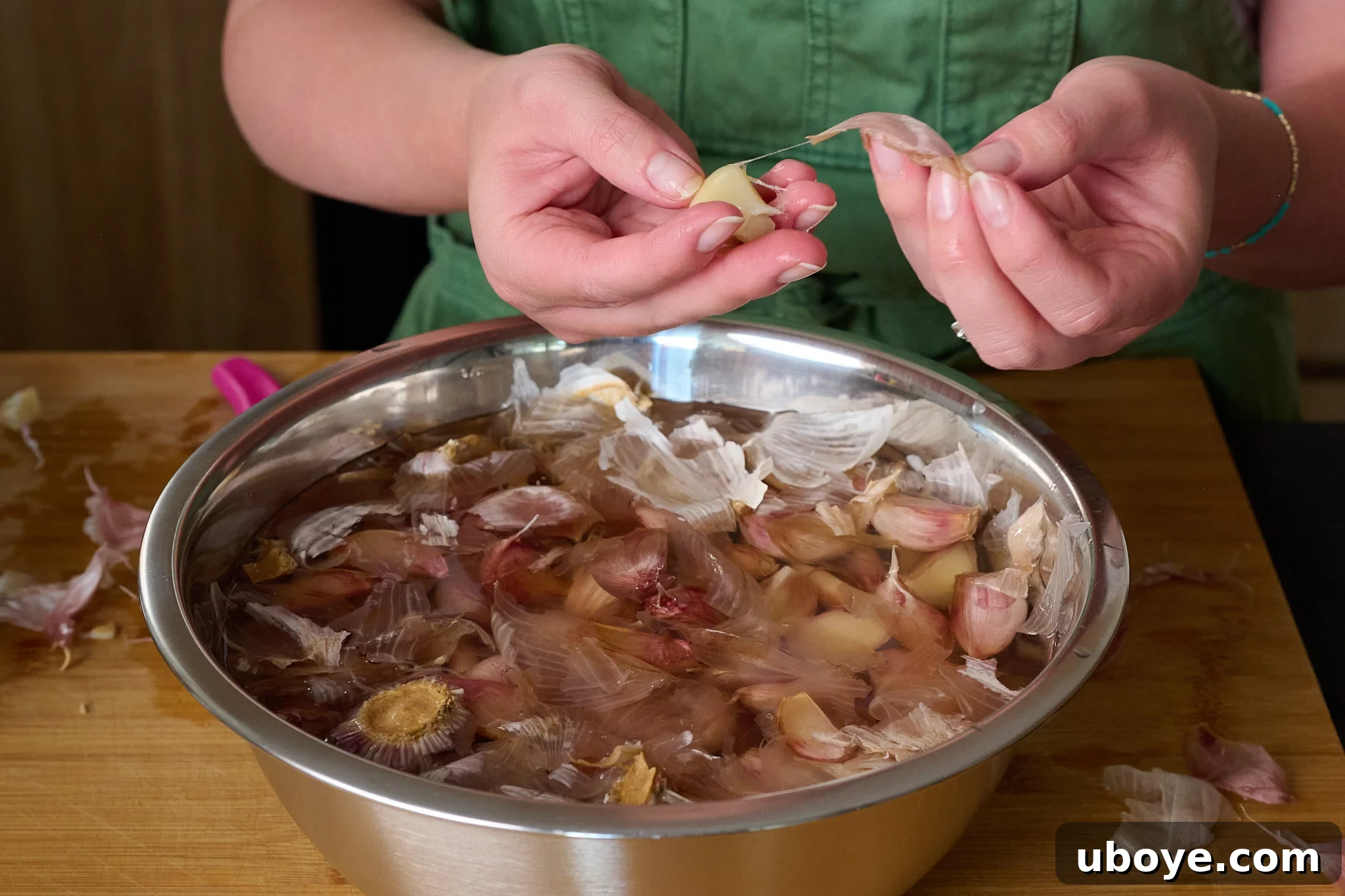 Garlic cloves partially submerged in water, demonstrating one clove being easily peeled by hand after the hot water treatment.