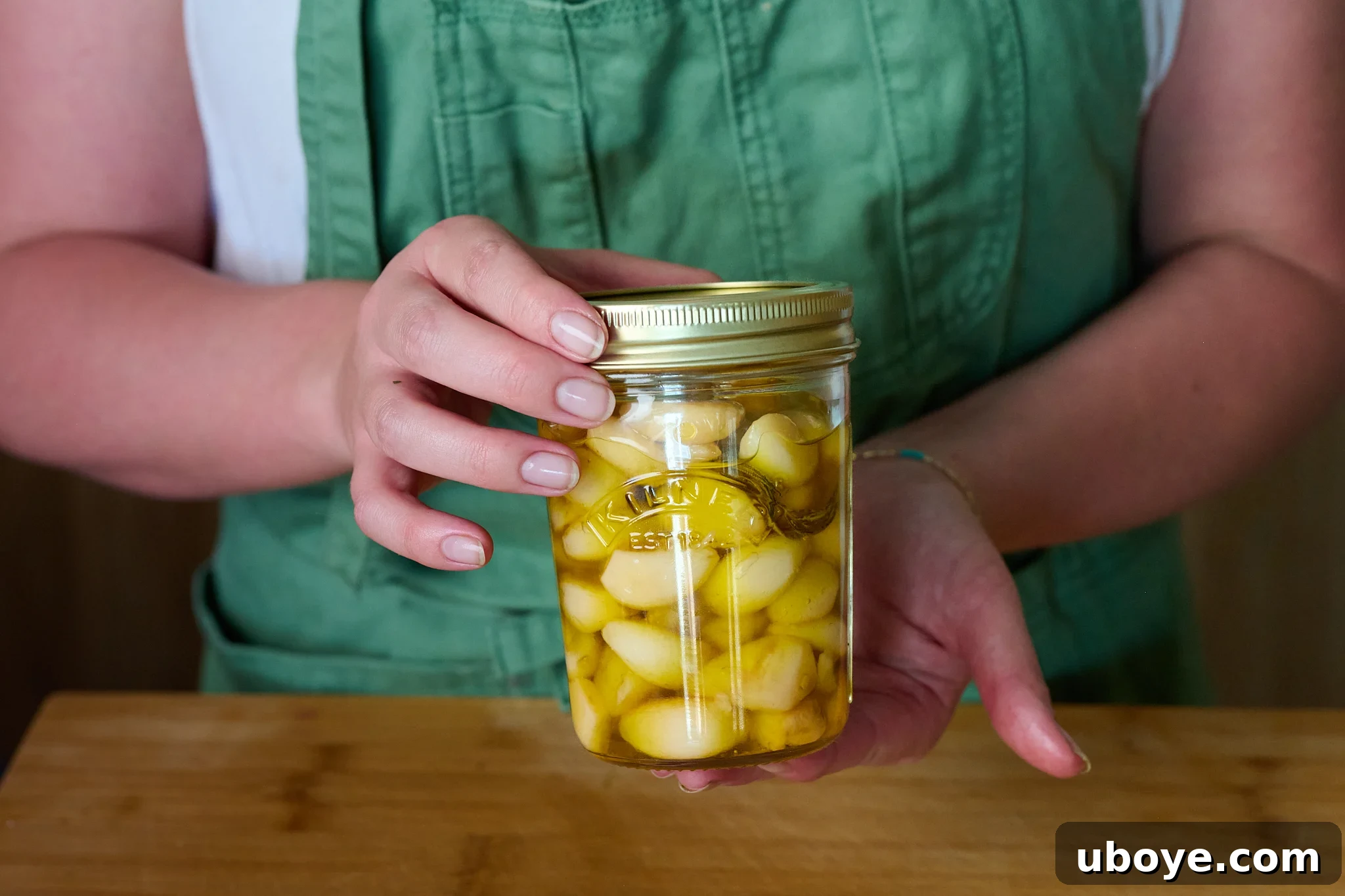 Cooked golden garlic confit cloves are carefully transferred into a clean glass jar, then completely covered with the flavorful garlic-infused olive oil for storage.