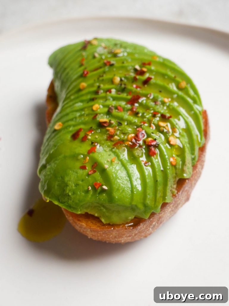 A perfectly prepared slice of avocado toast, richly green avocado spread on golden-fried sourdough, topped with chili flakes, salt, and pepper.