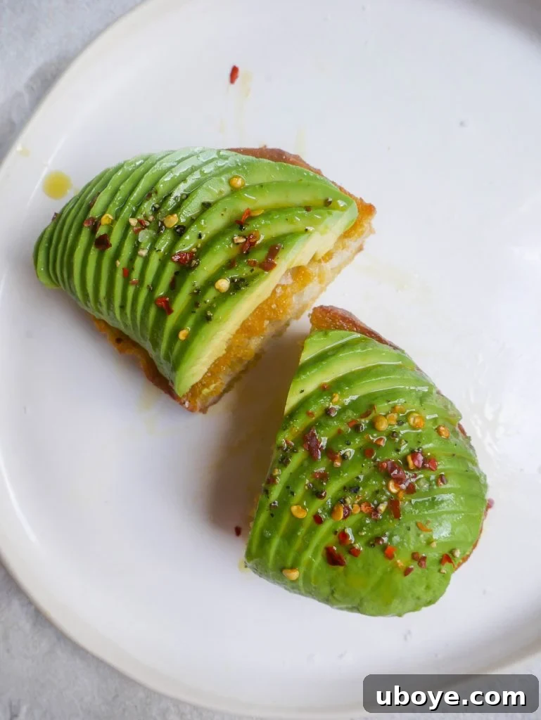 Close-up of a hand drizzling olive oil over a freshly prepared avocado toast, highlighting the glossy finish and vibrant green avocado.