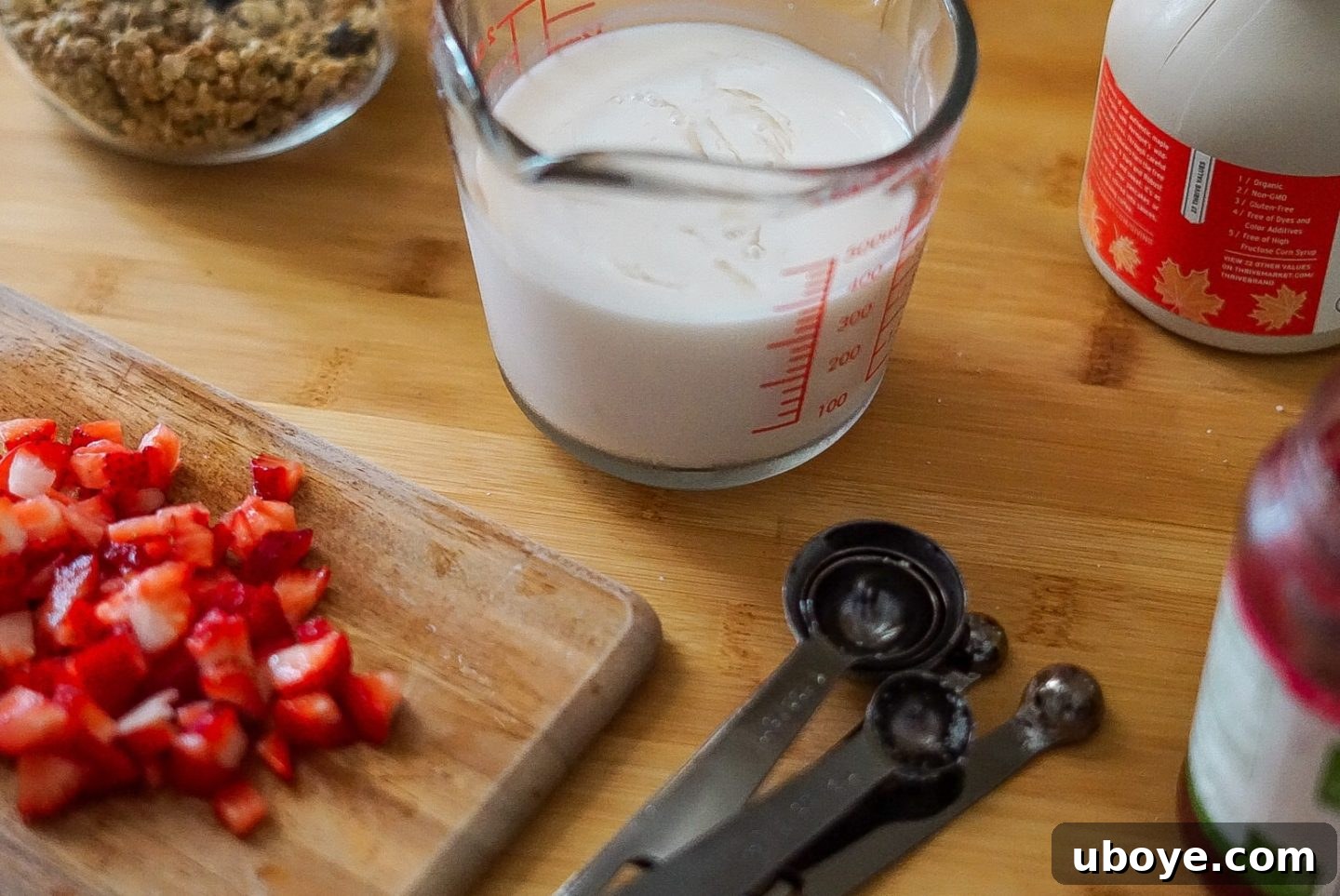 An array of fresh ingredients for baking muffins, including bananas, strawberries, oats, and almond milk, neatly arranged on a kitchen counter