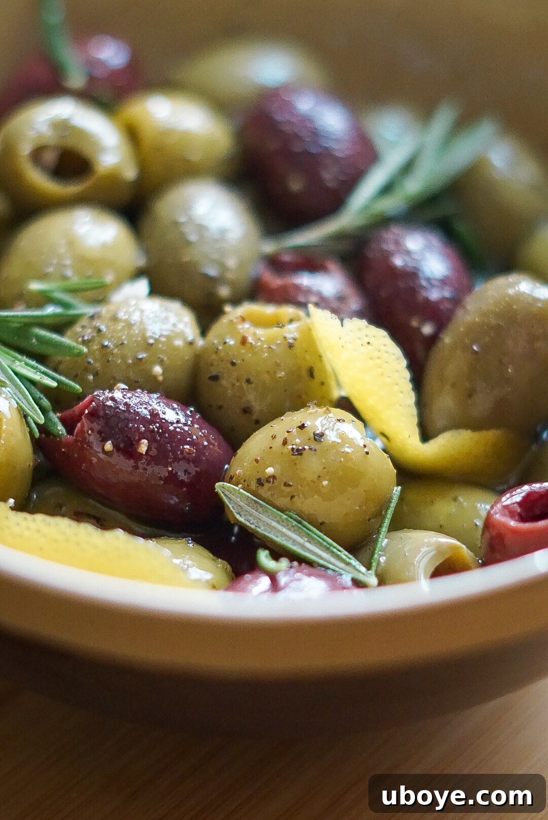 Herbed Mediterranean Olives 3 A close-up view of seasoned green and Kalamata olives, glistening with olive oil and speckled with herbs.