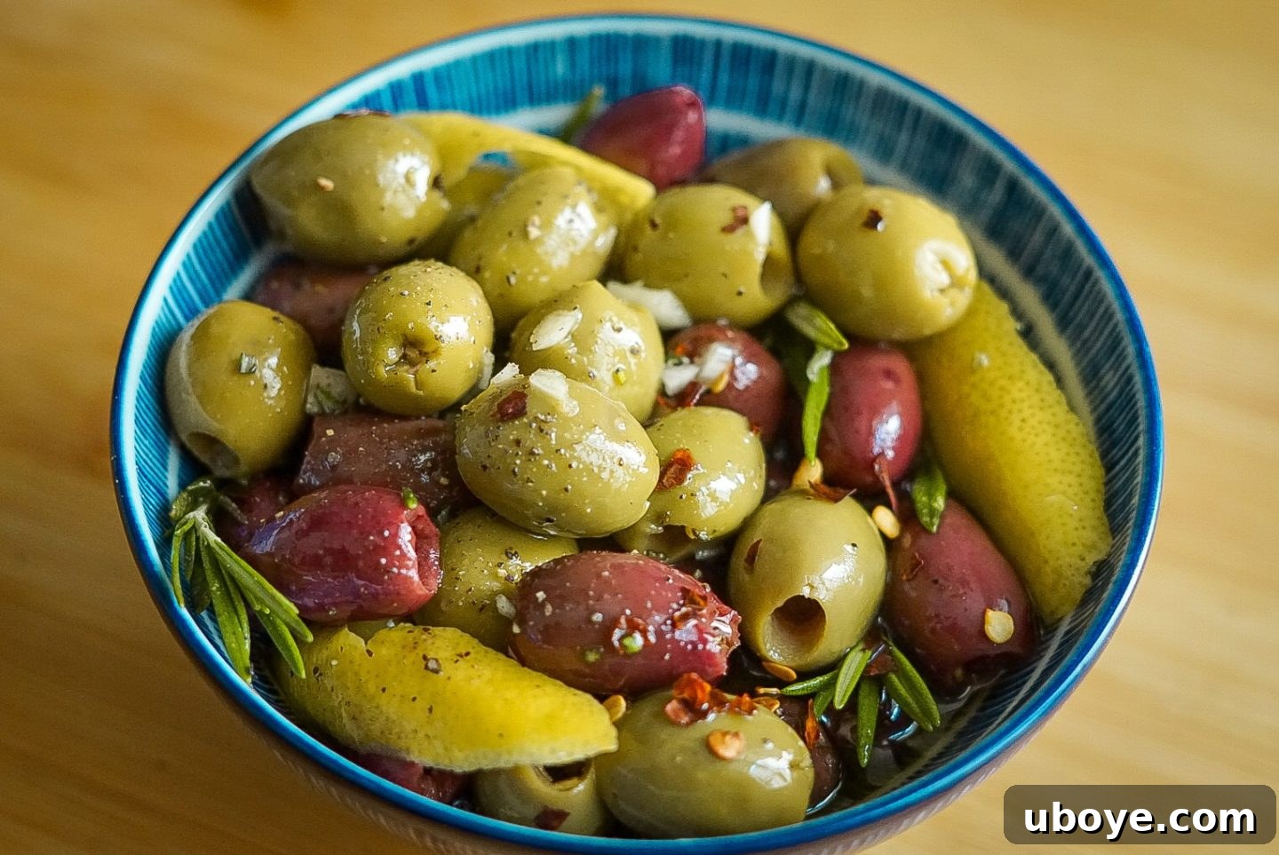 Herbed Mediterranean Olives 4 An overhead shot of a bowl of homemade marinated olives, garnished with fresh rosemary and lemon wedges.