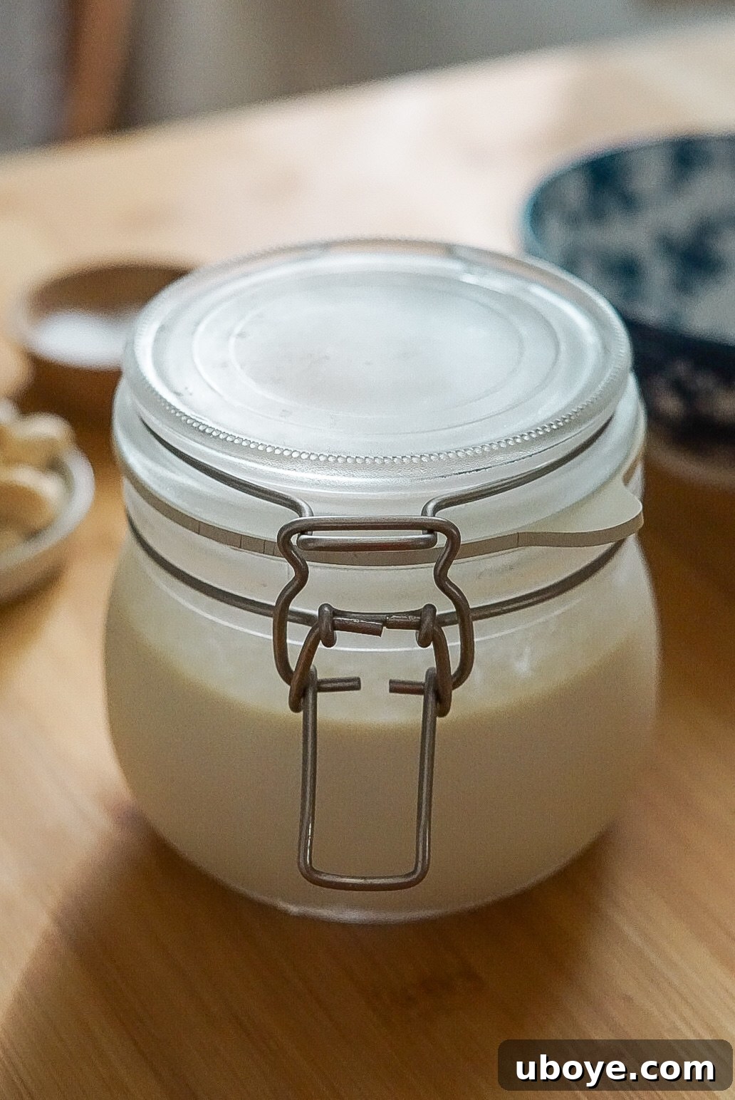 Container of homemade vegan sour cream with a wooden spoon, indicating it can be stored for about a week in the refrigerator.