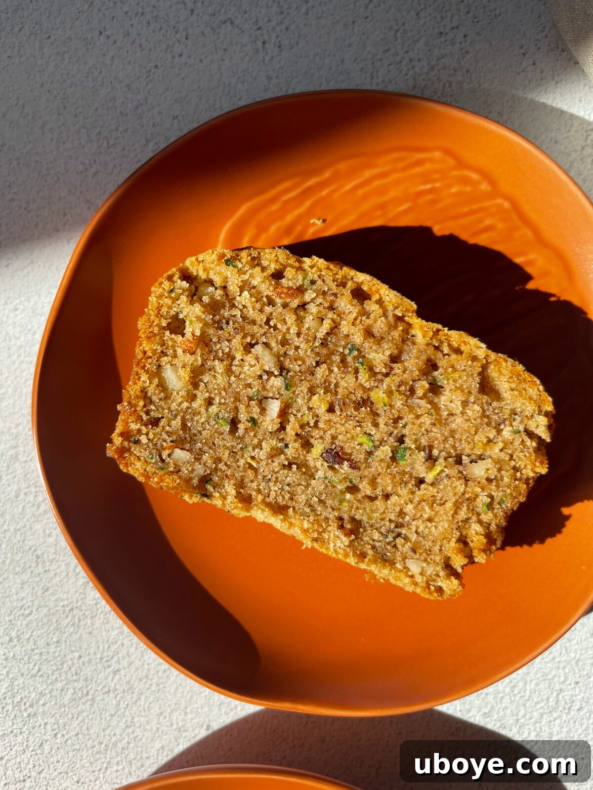 A generous slice of delicious vegan zucchini bread with pecans, served on a vibrant orange plate, ready to be enjoyed.