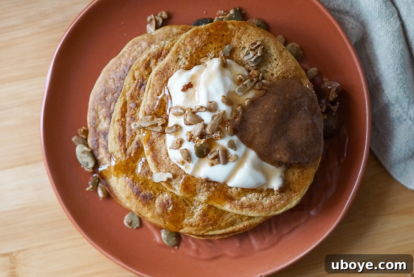 A close-up of a single vegan pumpkin pancake on a plate, adorned with a swirl of coconut yogurt and a pool of maple syrup, ready to be enjoyed.