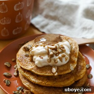 A top-down view of a stack of golden brown vegan pumpkin pancakes, lightly dusted with powdered sugar and ready to be served.