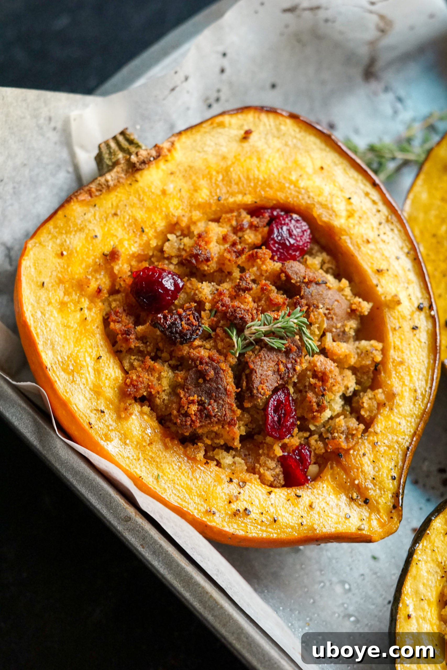 Two halves of golden-roasted stuffed acorn squash, brimming with a savory cornbread and sausage filling, garnished with fresh herbs.
