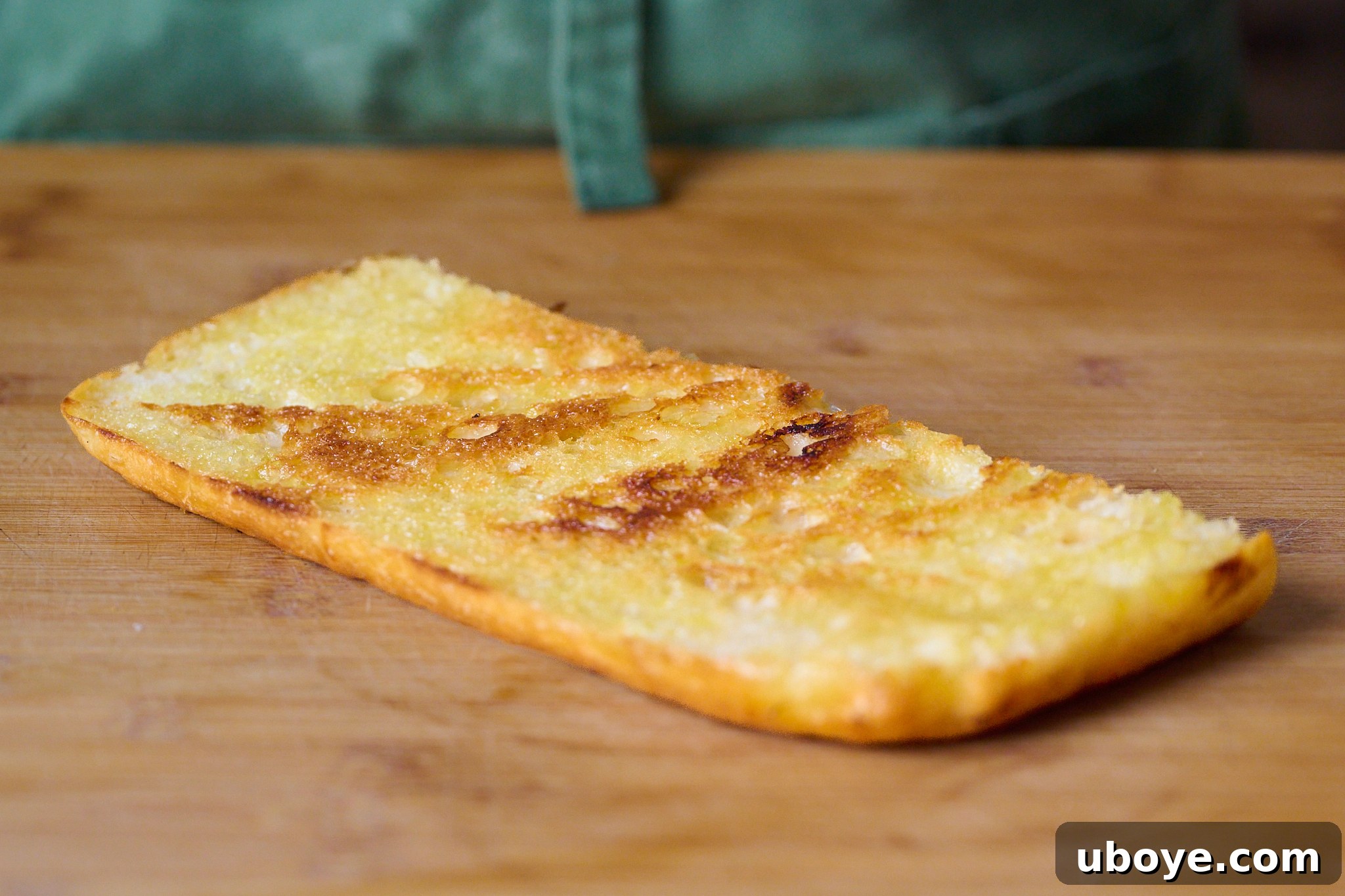 Piece of focaccia that has been slightly toasted. Sits on wooden chopping board. 
