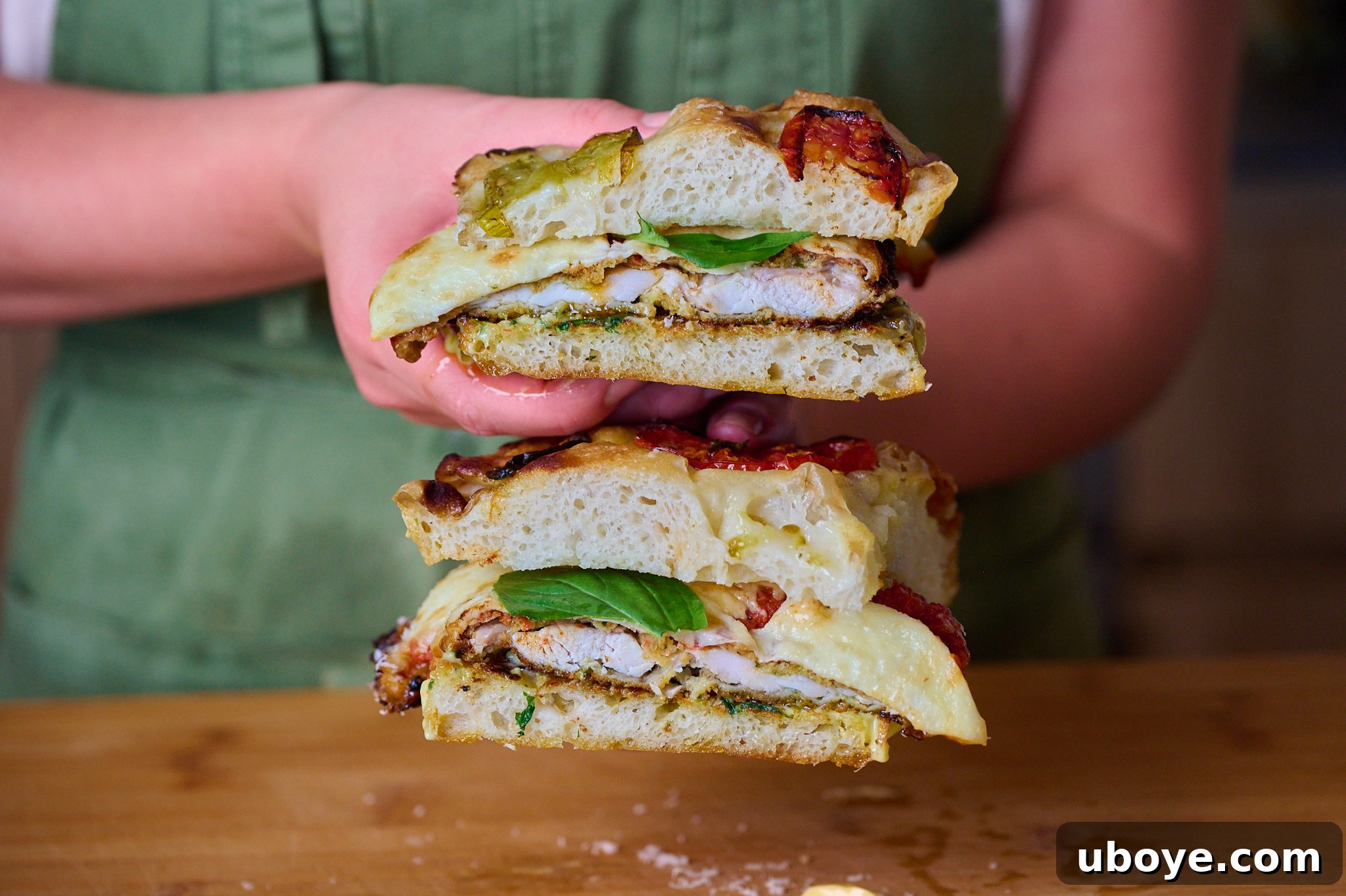 Chicken parm sandwich that has been sliced in half and is being held by cook with green apron. You can see all elements of the sandwich in this photo. 