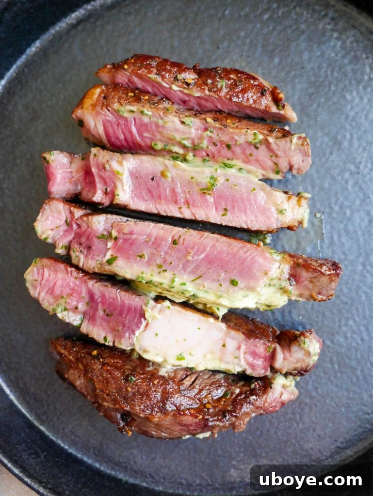 Slices of perfectly cooked steak arranged on a cutting board, each piece adorned with a dollop of garlic confit herb butter, ready for serving.