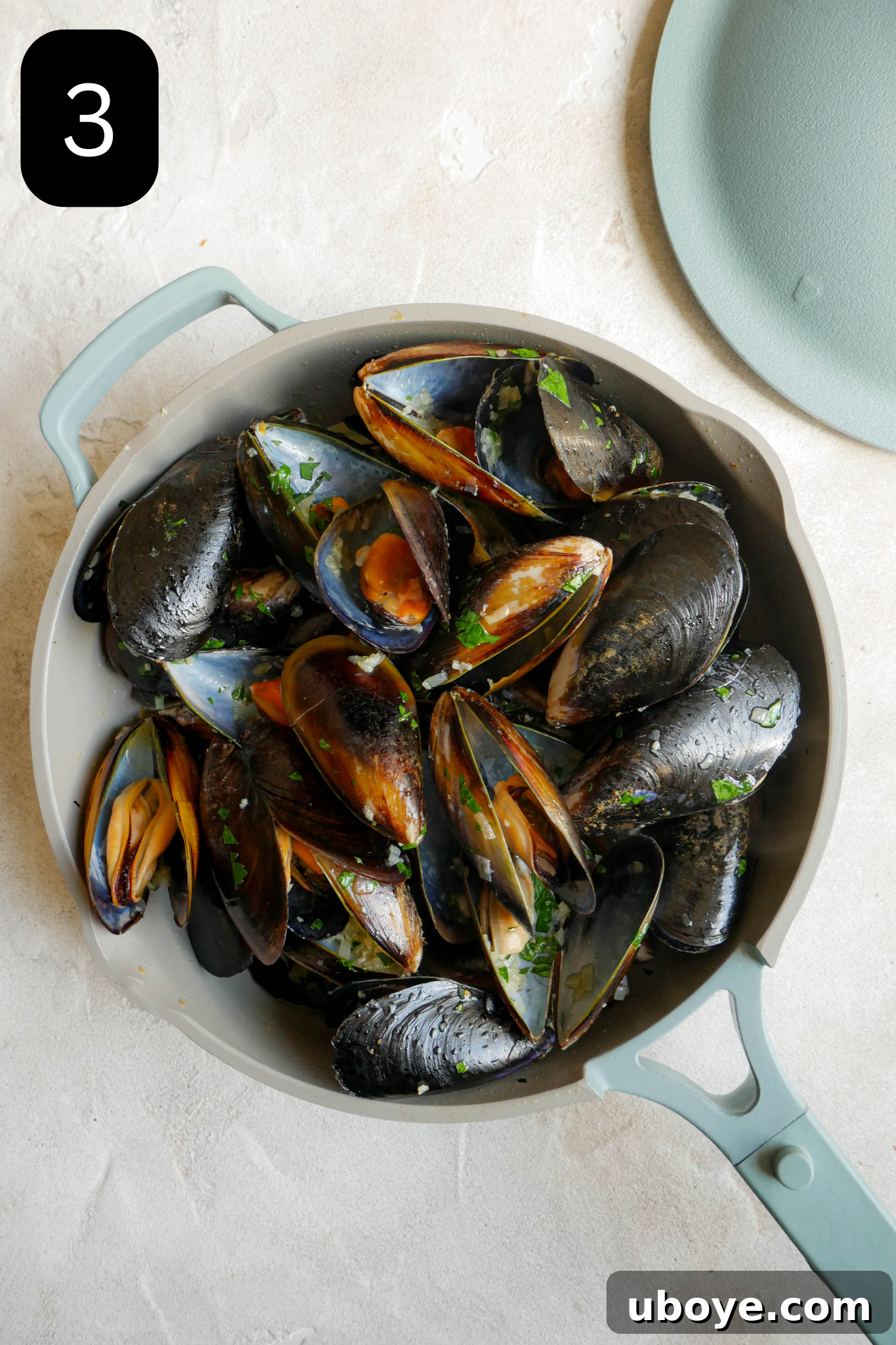 Aromatic White Wine Butter Mussels 6 A deep blue pot filled with mussels being steamed in the white wine butter sauce, with the lid placed slightly ajar on the side.