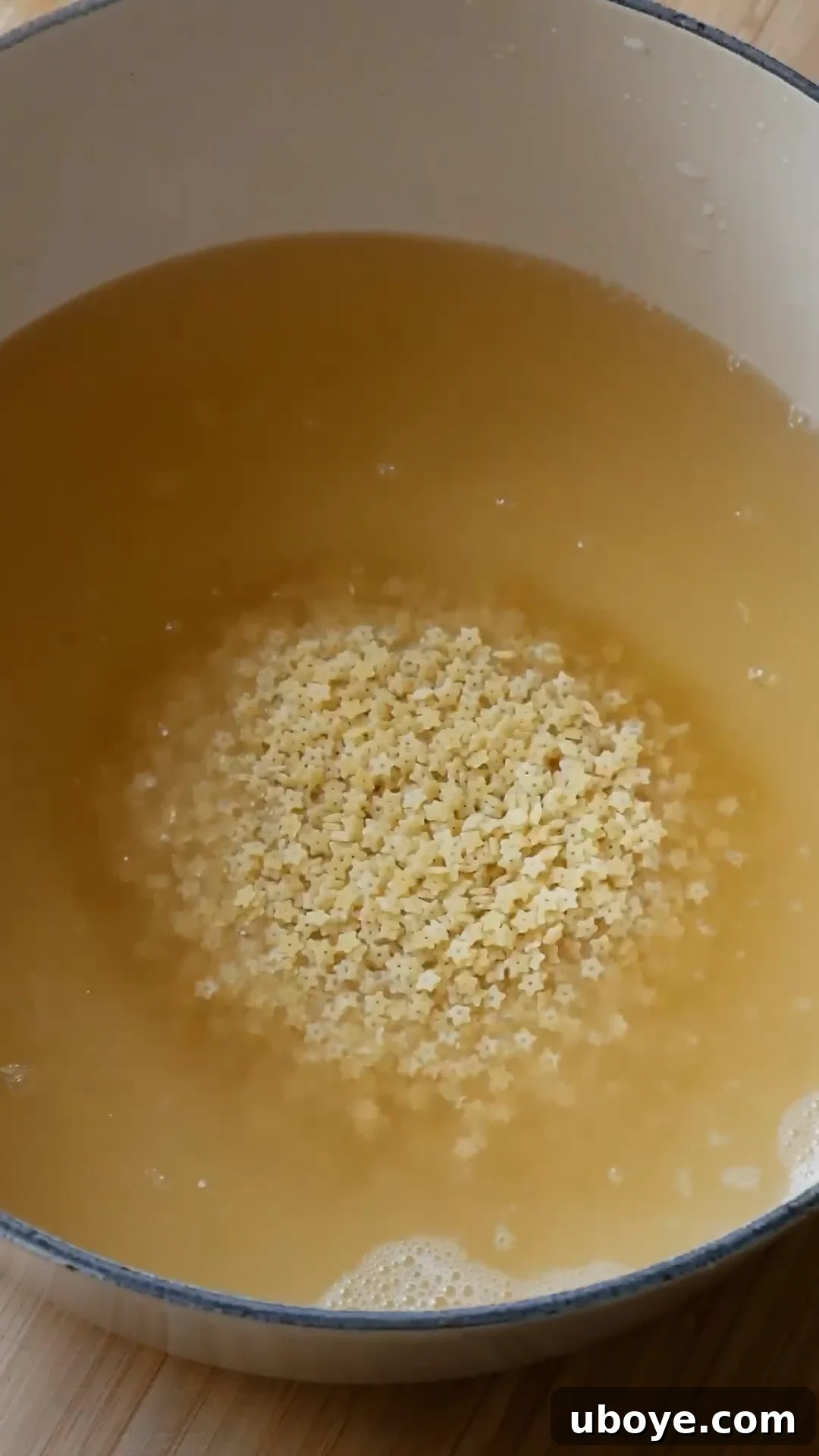 Uncooked pastina being added to boiling chicken broth in a pot.