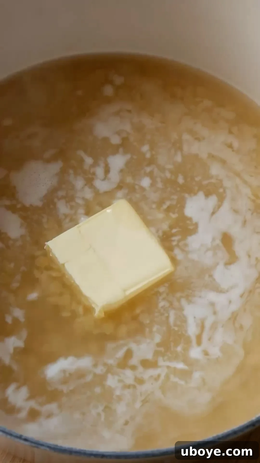 Butter being stirred into the pot with pastina and chicken broth as it simmers.