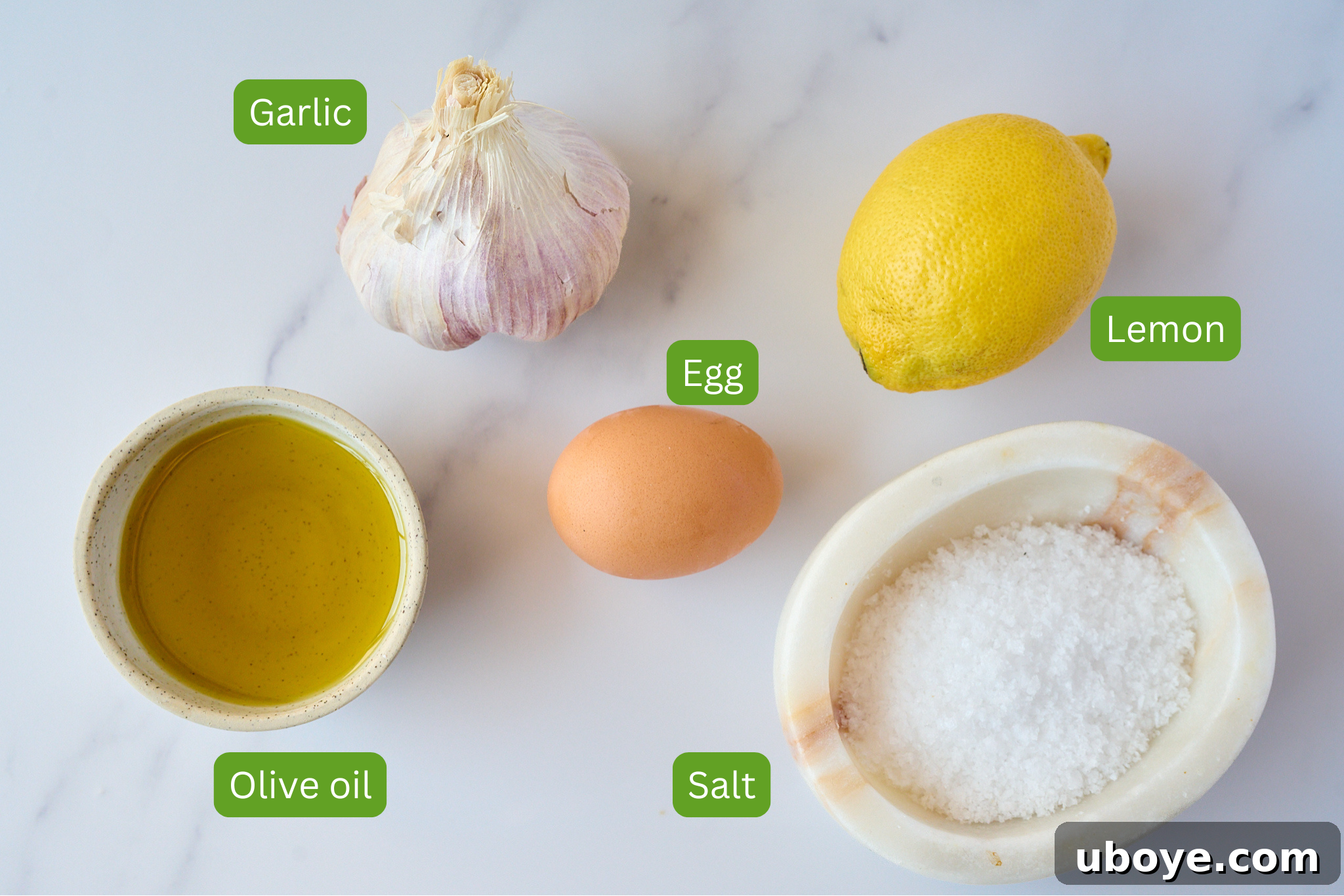 Close-up shot of the fresh ingredients for garlic confit aioli: olive oil, lemon, garlic confit, egg, and sea salt.