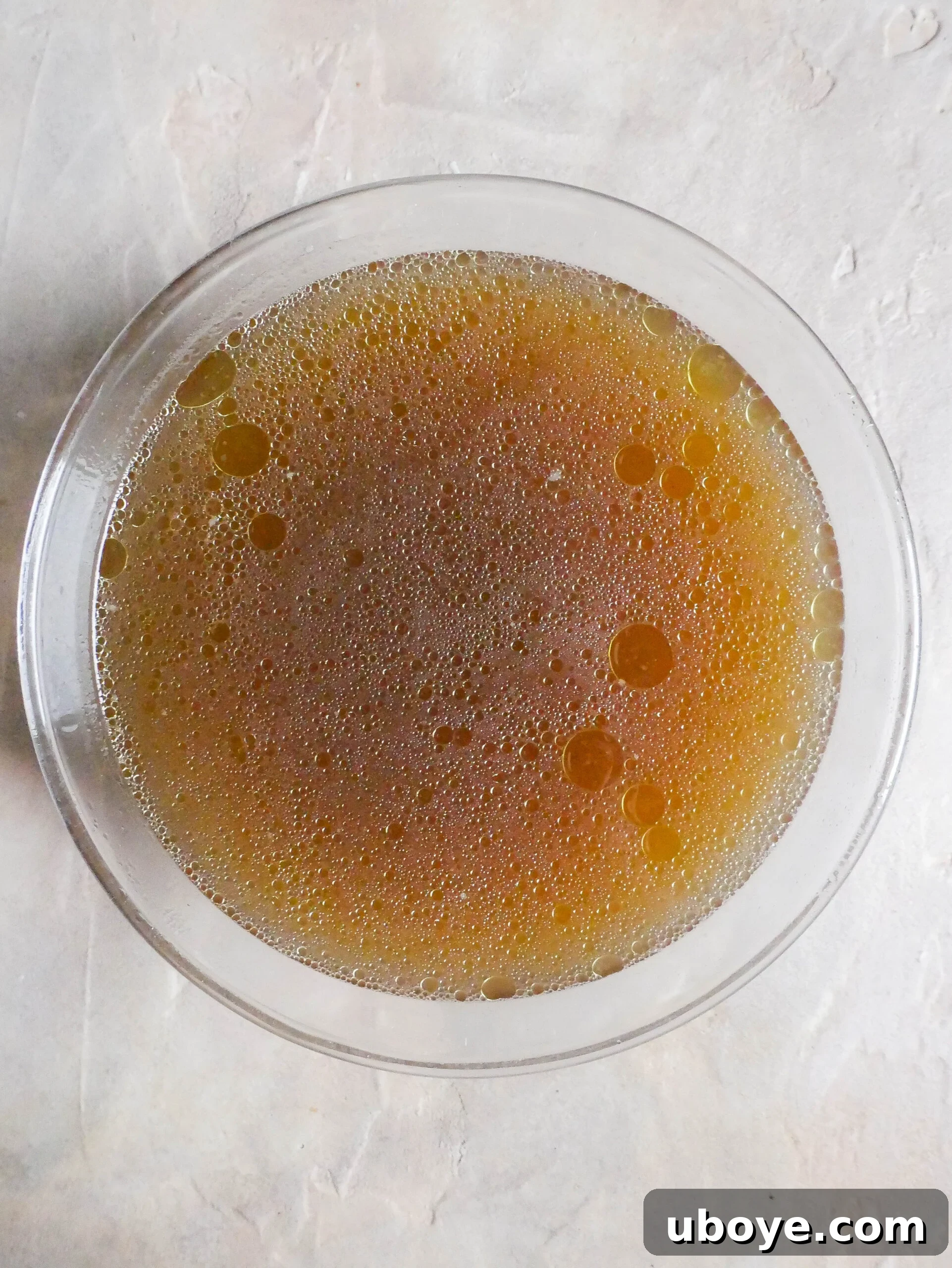 Clear, golden strained chicken broth in a glass bowl.