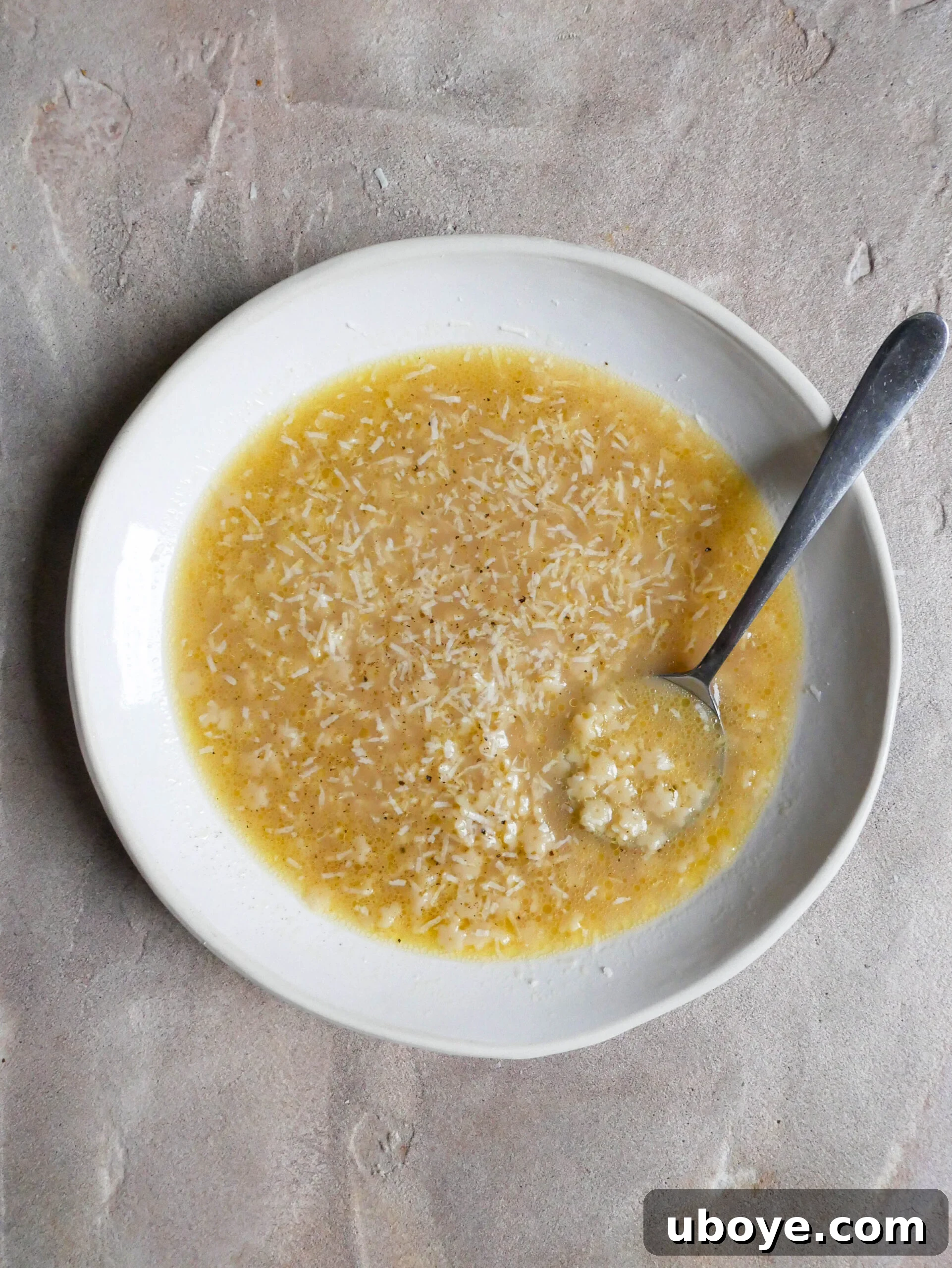 A bowl of pastina in chicken broth, topped with grated cheese, and a small cheese grater next to it.