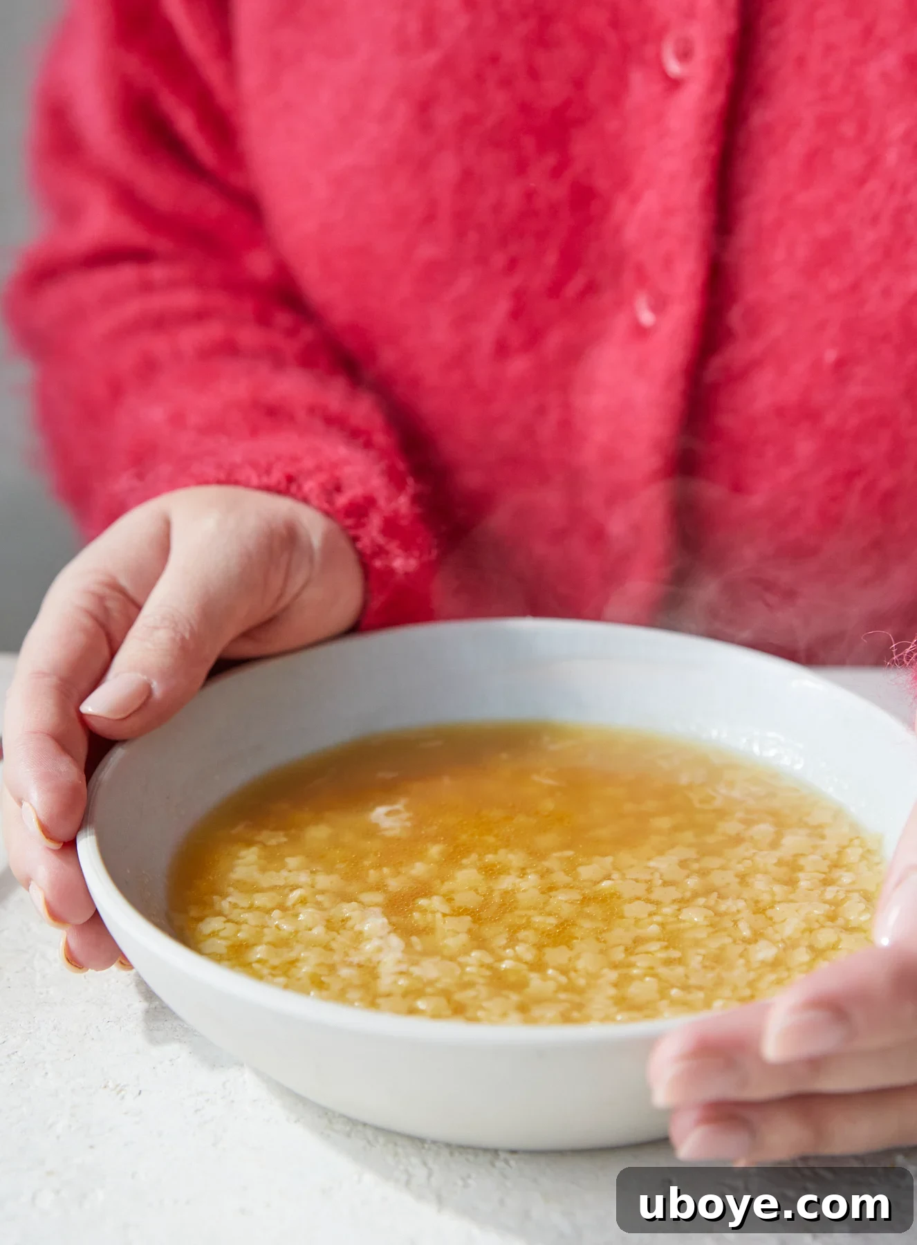 A person in a pink fluffy jumper gently holds a bowl of Pastina in Chicken Broth, emphasizing its comforting nature.
