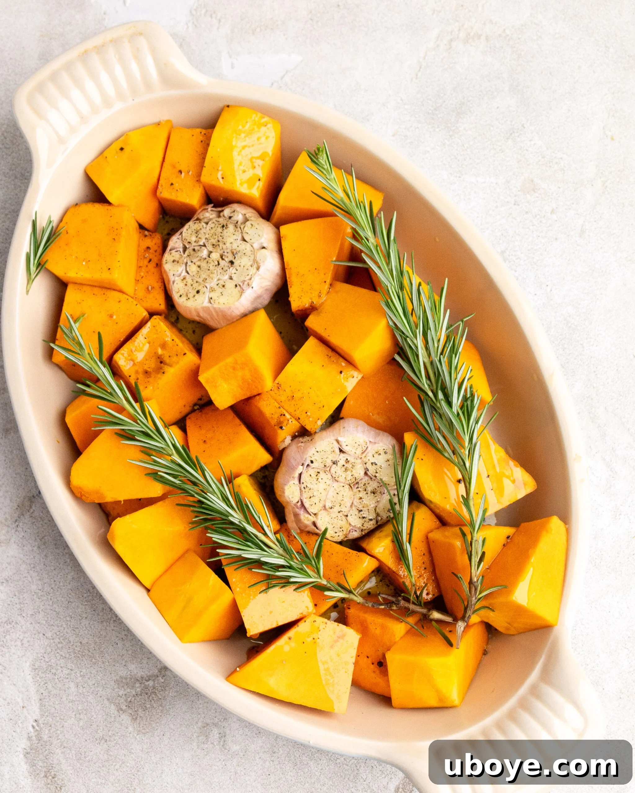 Raw pumpkin, garlic, and rosemary are neatly arranged in a baking dish, ready for roasting.
