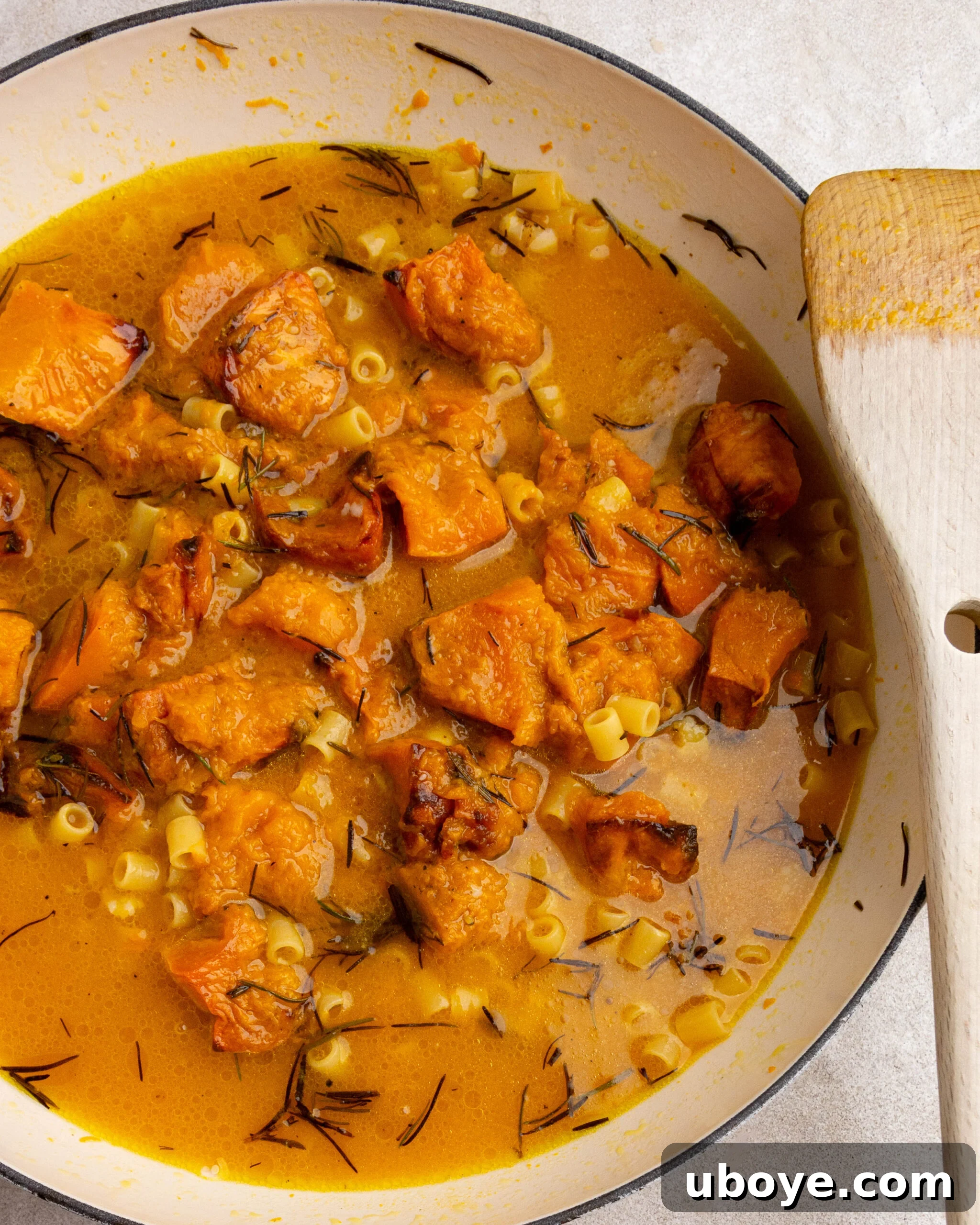 Roasted pumpkin, broth, and pasta are simmering together in a large white pan on the stovetop.