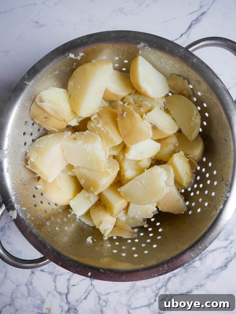 Diced potatoes steaming in a colander after parboiling, being gently roughed up with a spoon