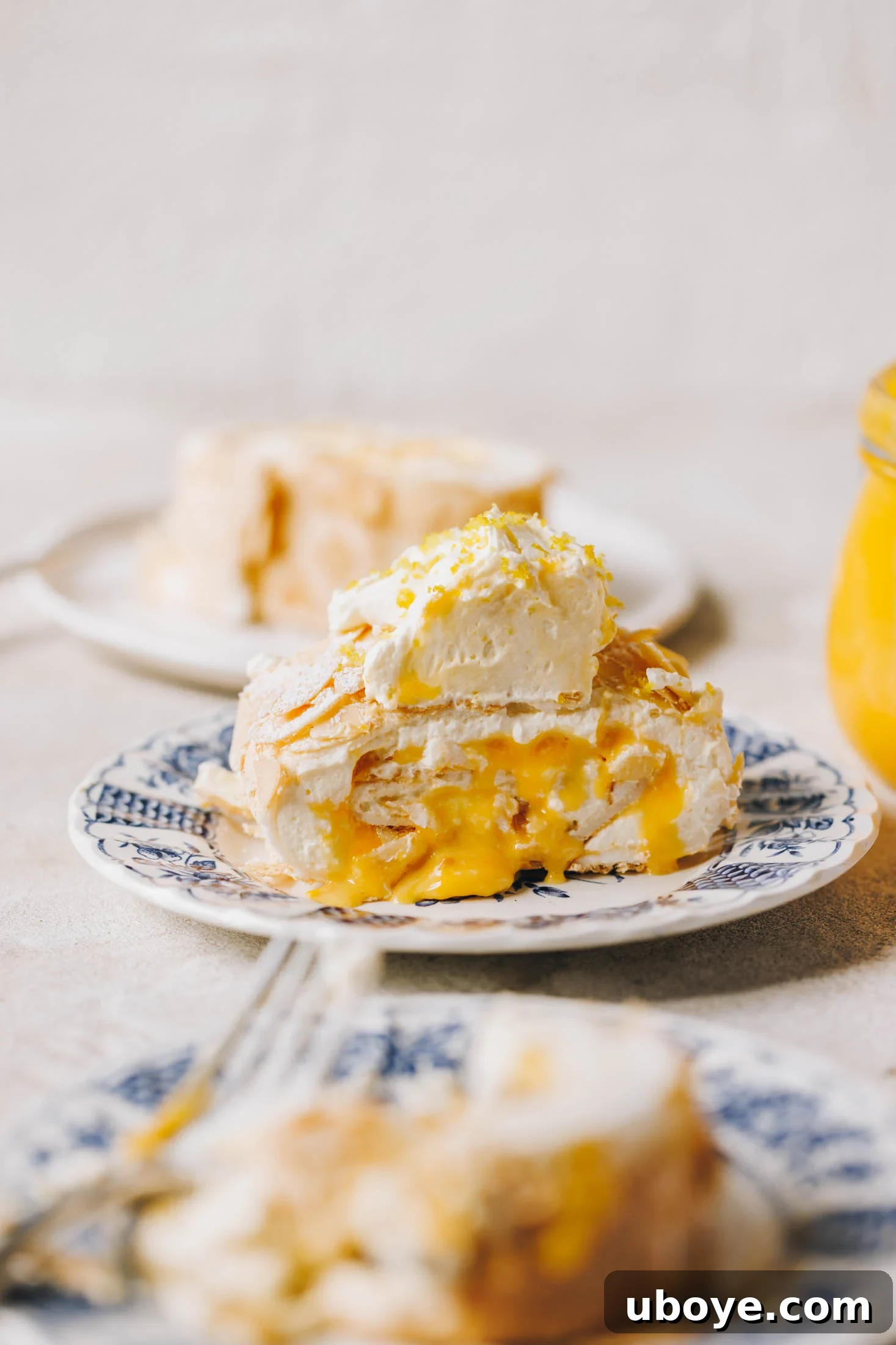 A slice of lemon curd meringue roulade sits on a blue and white plate with a floral pattern. 