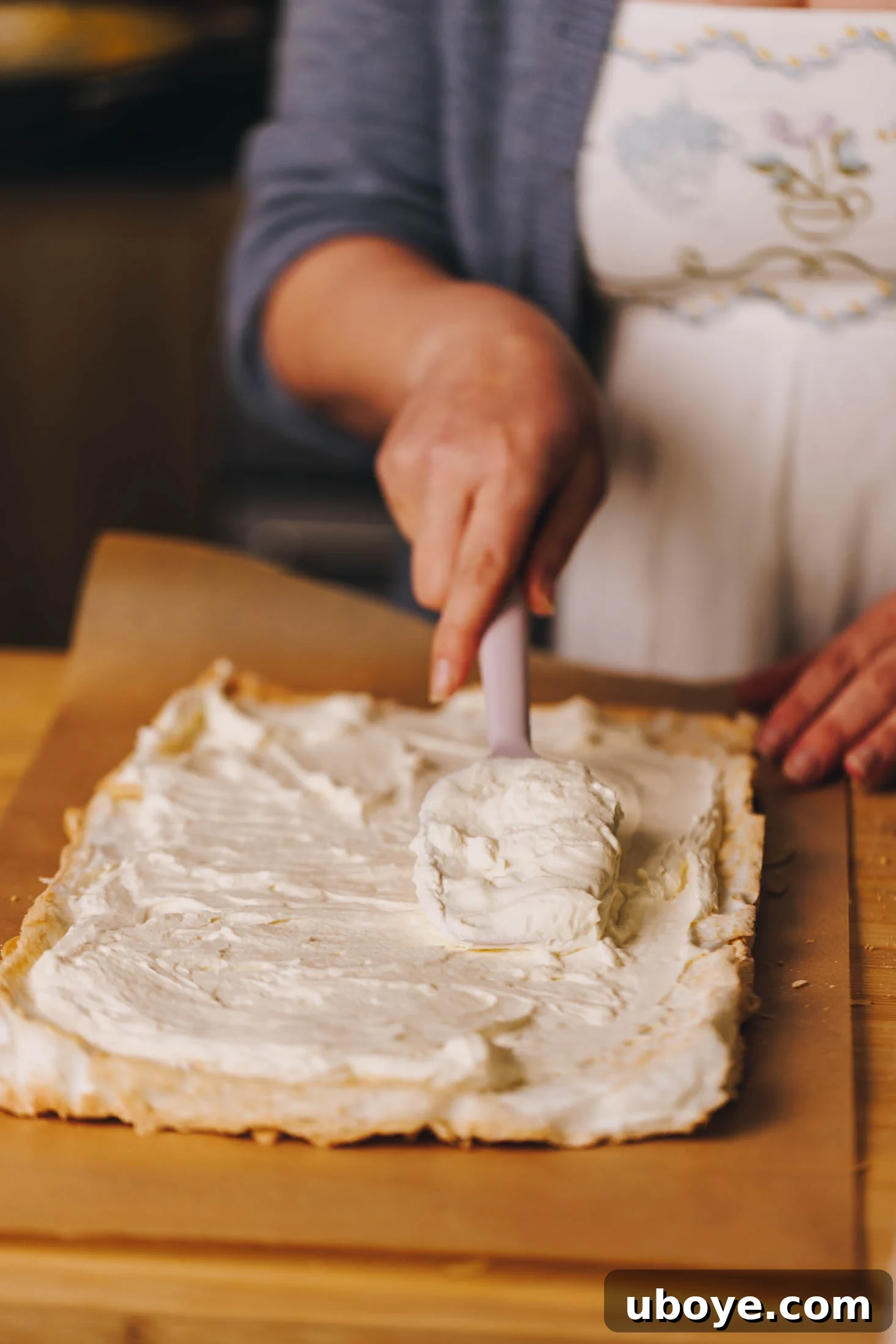Cooked meringue has been remove from baking tray and is being layered with whipped cream. 