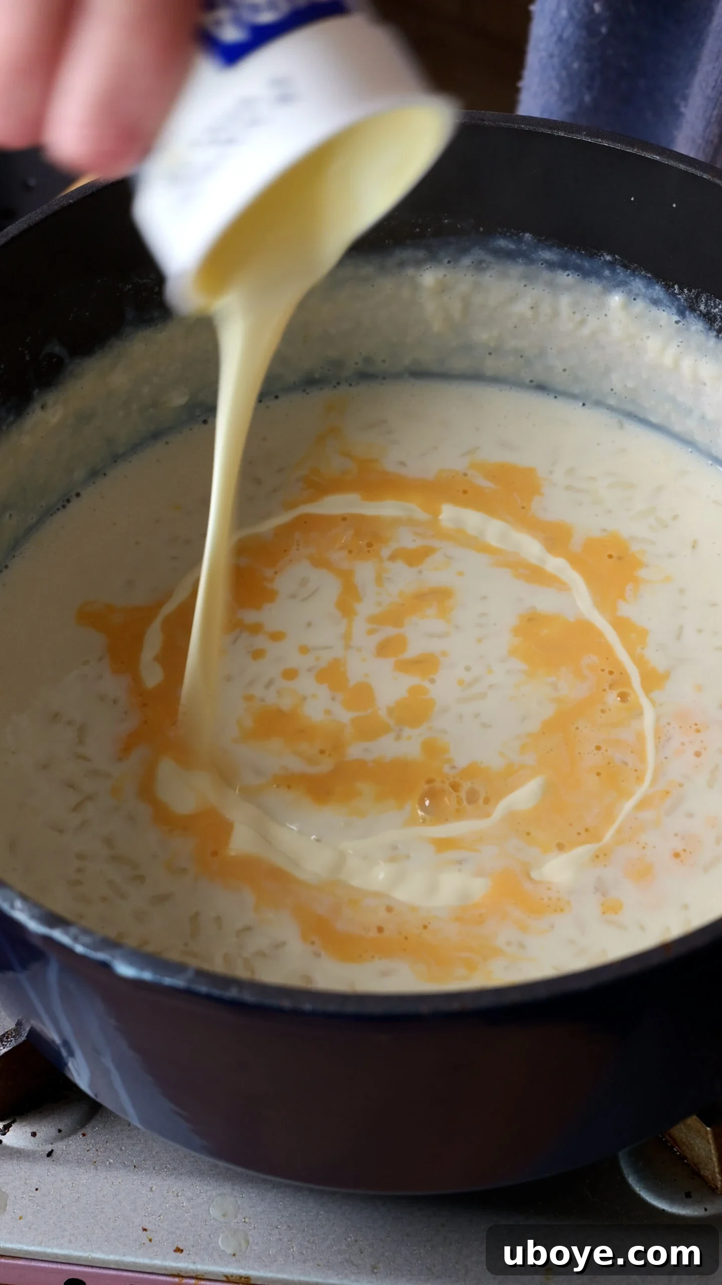 Abuelo's Arroz con Leche Spanish Rice Pudding 6 The tempered egg yolk mixture and thickened cream being carefully poured into the large blue pot of cooked rice pudding, ready for final simmering.