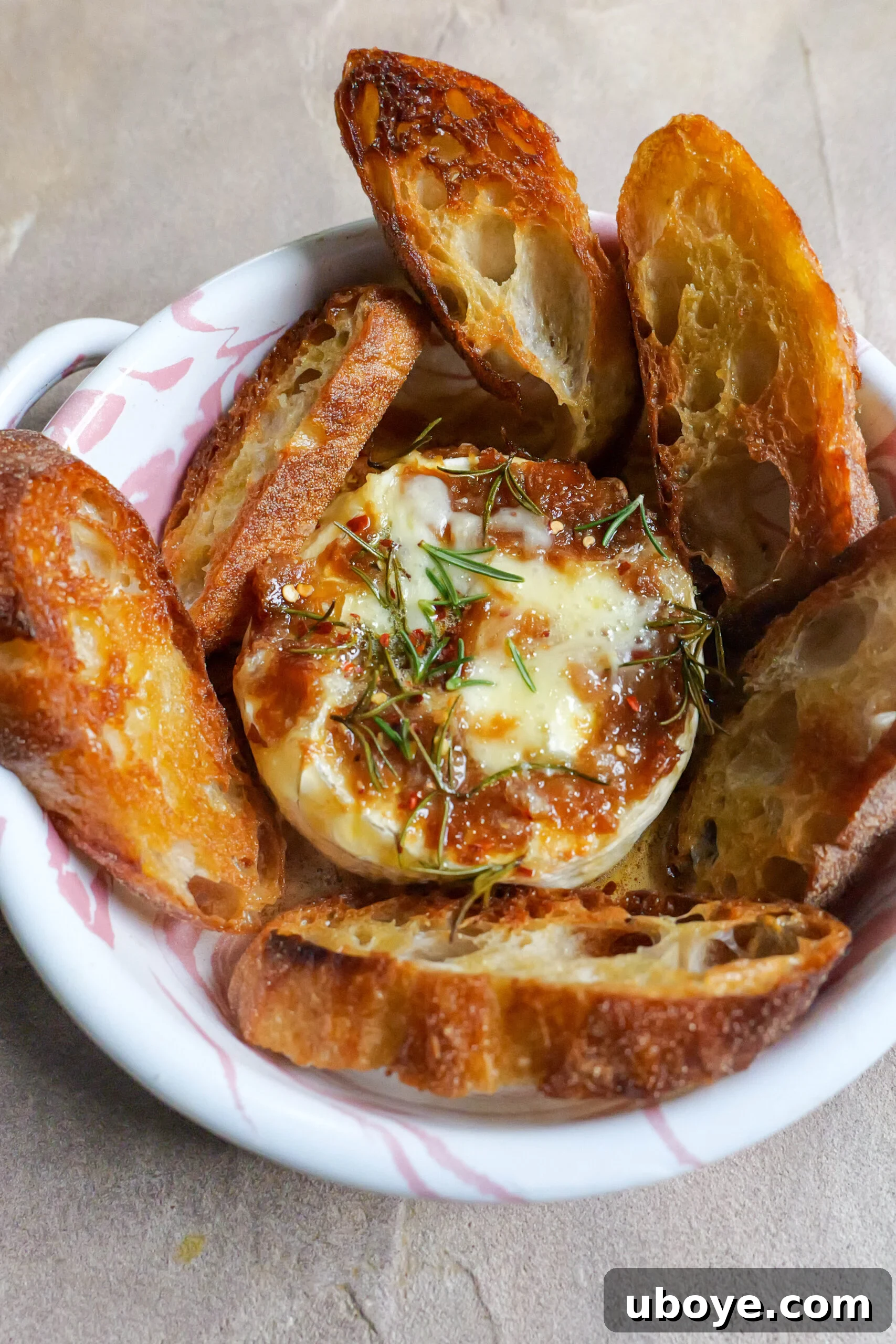 Holiday Roasted Garlic Butter Baked Brie 2 Baked brie with roasted garlic butter sits in pink and white tray with olive oil fried slices of baguette