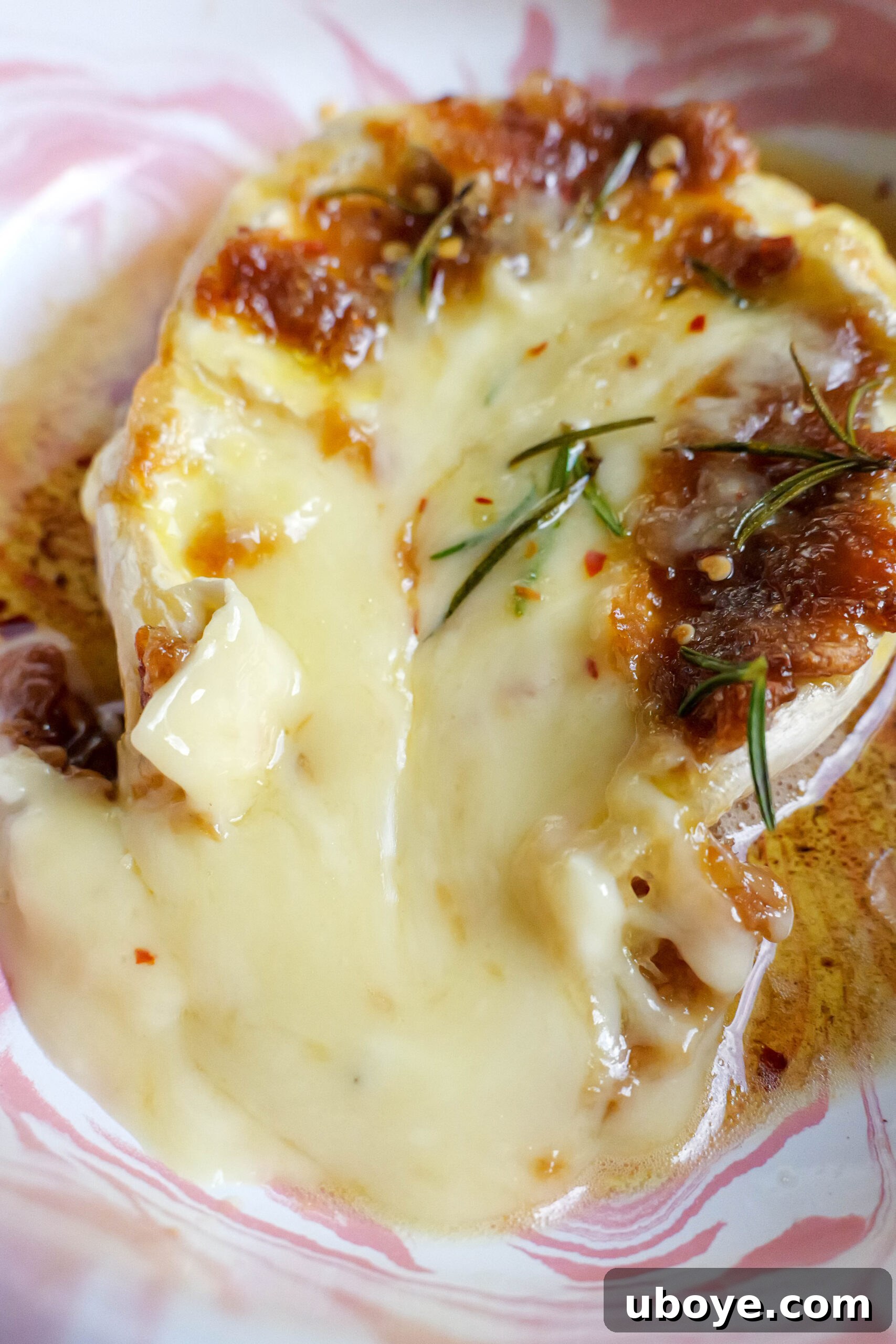 Holiday Roasted Garlic Butter Baked Brie 6 Baked brie with roasted garlic butter sits in pink and white tray. The brie has been cracked open and is oozing into the tray.