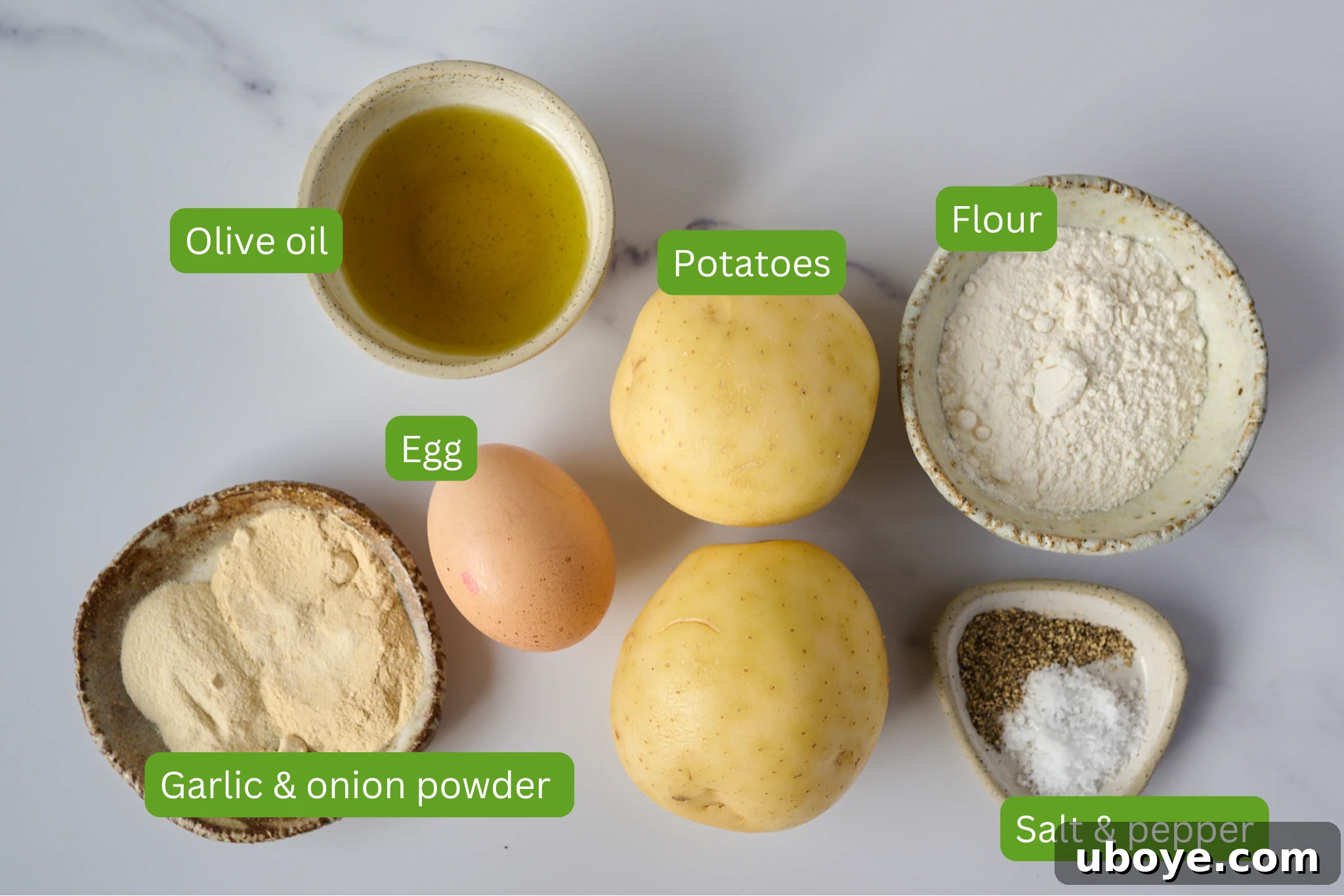Golden Crispy Potato Rosti 3 A flat lay photograph displaying all the ingredients for potato rosti: potatoes, flour, garlic and onion powder, salt, pepper, egg, and olive oil, arranged on a white marble background.