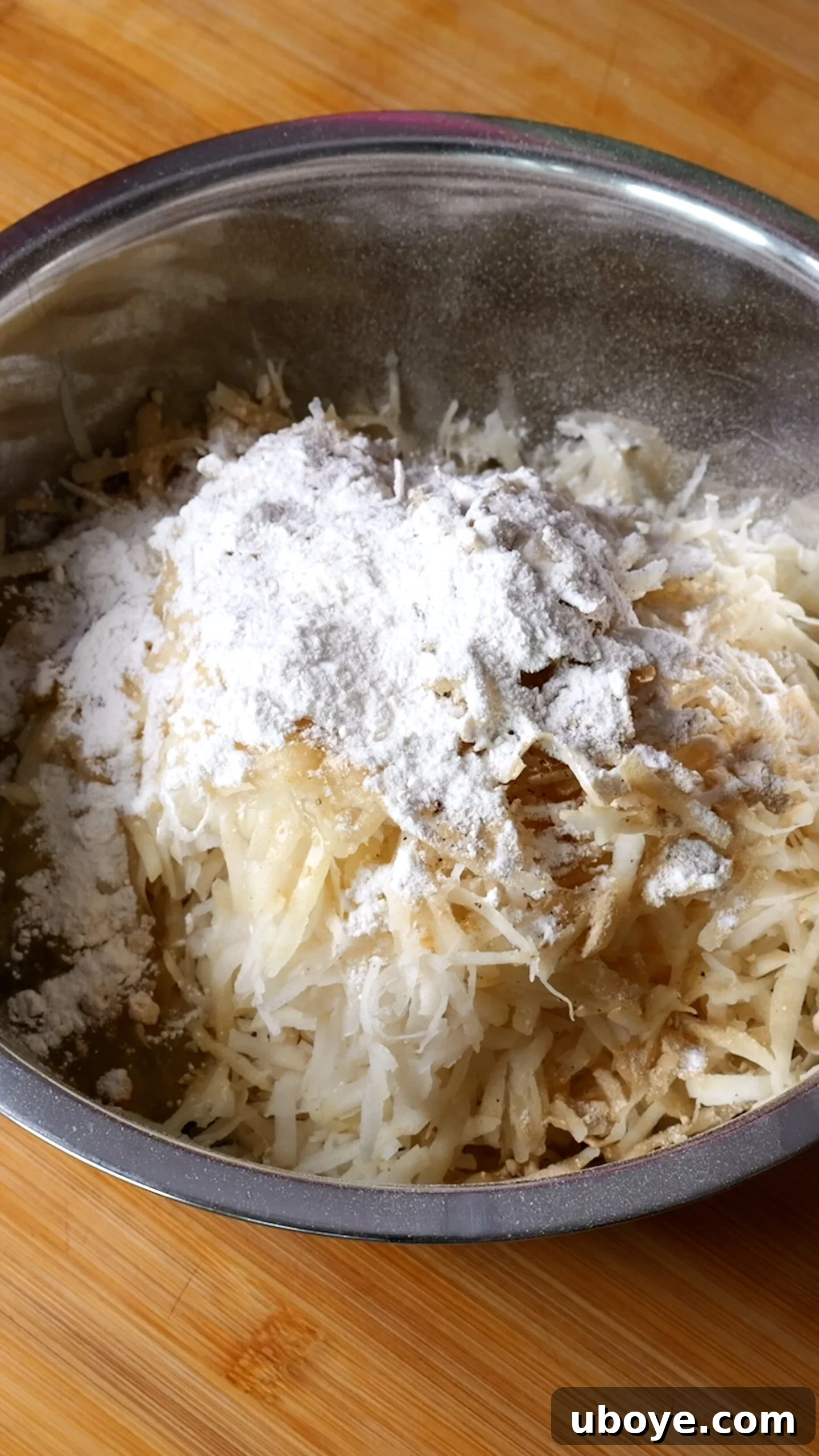 Golden Crispy Potato Rosti 8 Squeezed grated potatoes in a metal mixing bowl, seasoned with flour, egg whites, garlic and onion powder, salt, and pepper.
