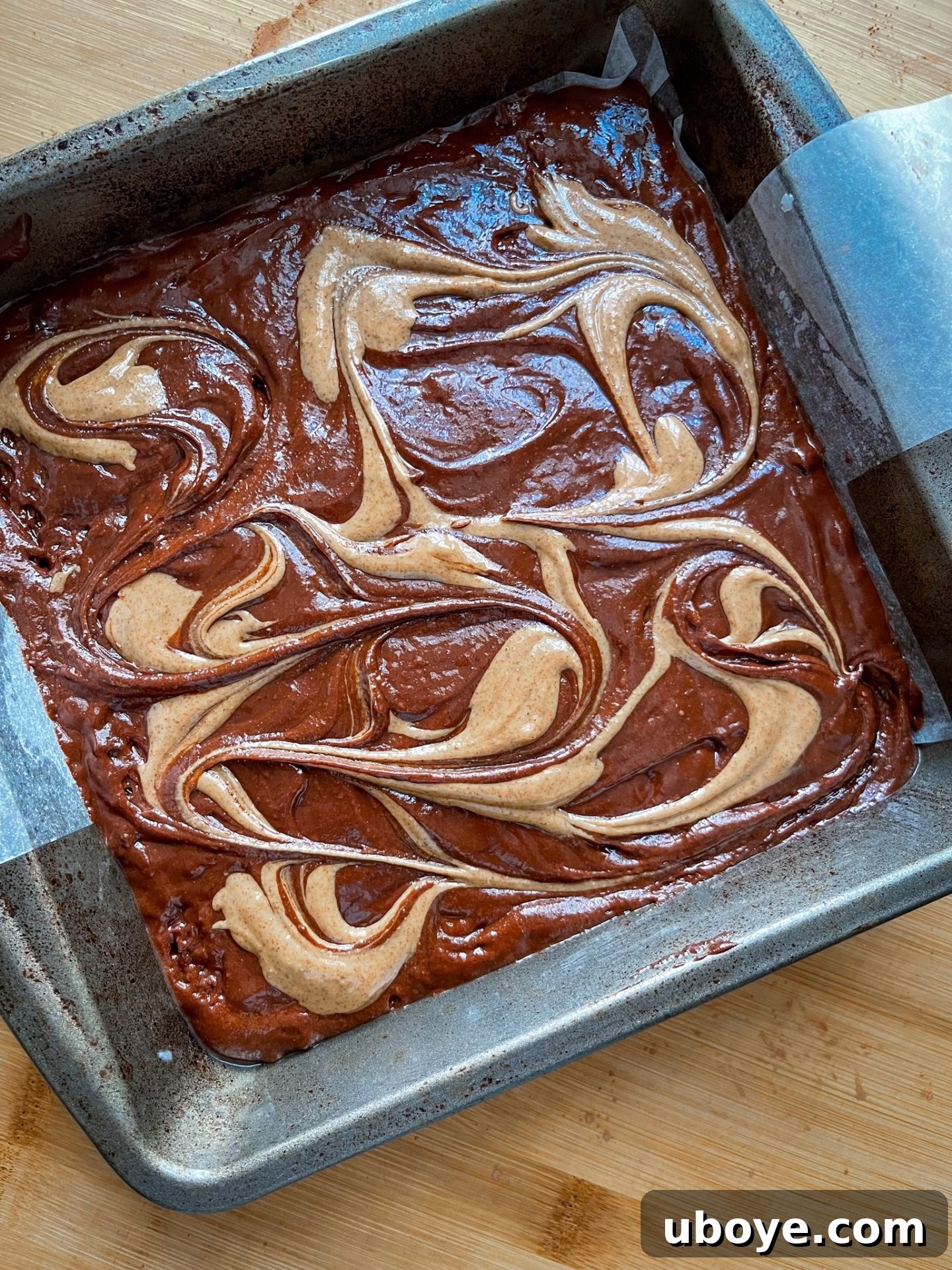 Unbaked vegan brownie batter with almond butter dots ready to be swirled for a decorative top
