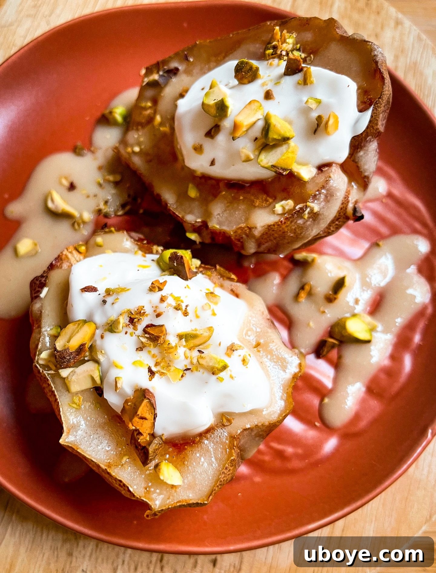 A close-up of air fried pear halves, with one drizzled with the maple miso tahini sauce and topped with coconut yogurt and pistachios.