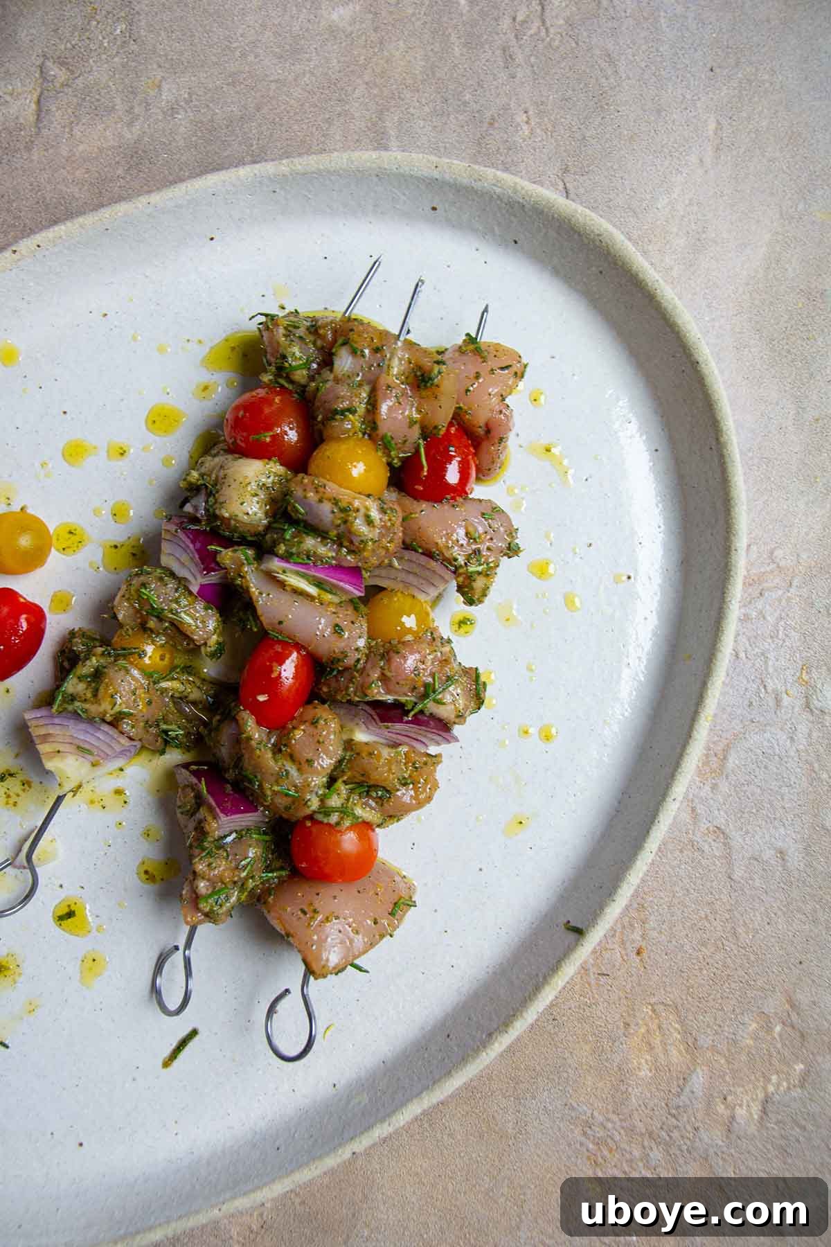 Three chicken skewers drizzled with olive oil on a white plate, garnished with fresh herbs.