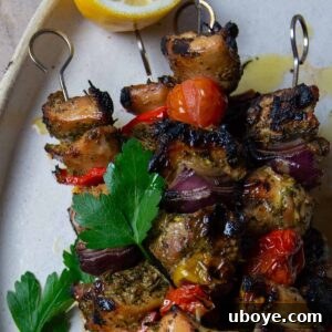 White plate of chicken skewers with parsley and half of a lemon.