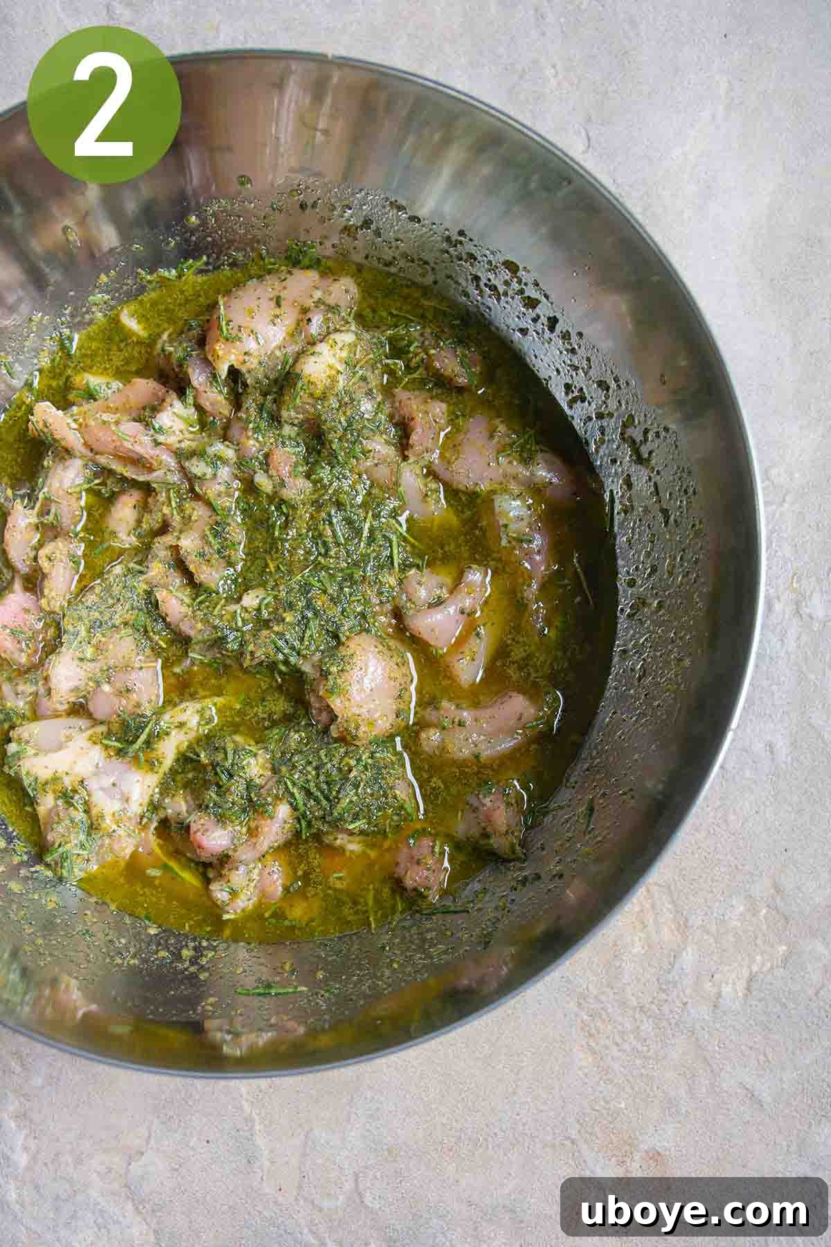 Cubed chicken thighs being mixed with the herb marinade in a bowl.