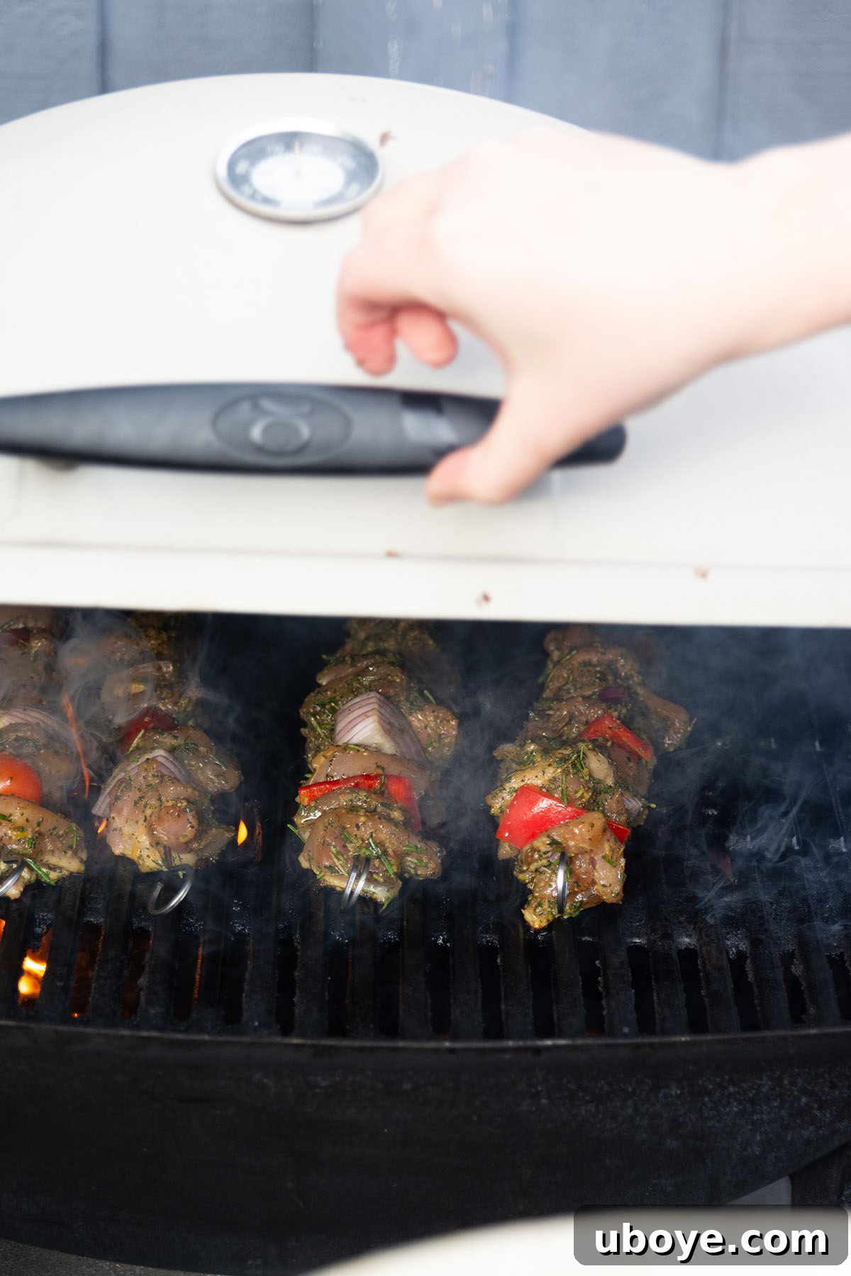 Opening a barbecue grill to reveal perfectly cooked Mediterranean chicken skewers.