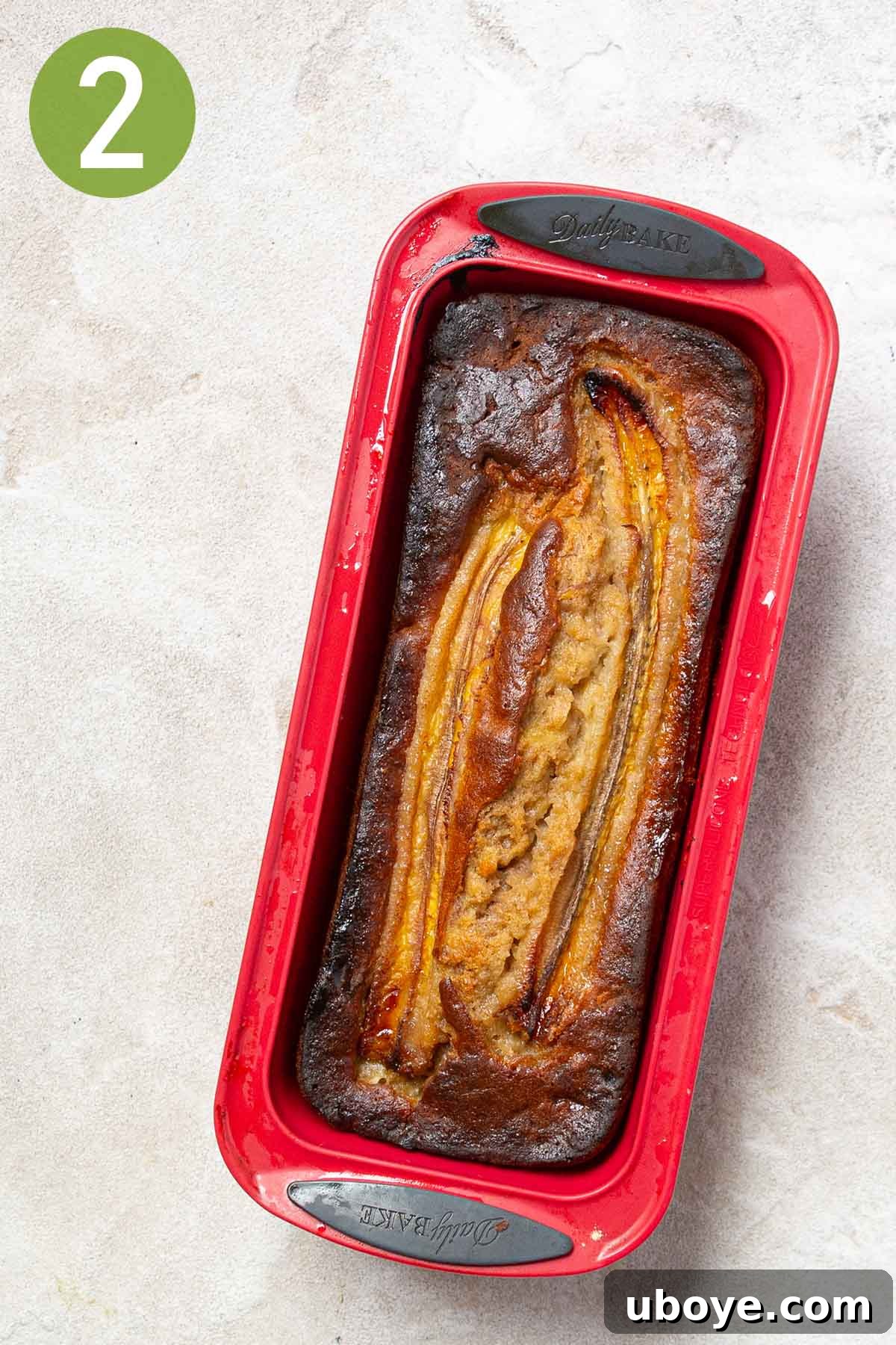 Freshly baked olive oil banana bread in a red loaf pan, golden brown and perfectly risen, cooling on a wire rack.